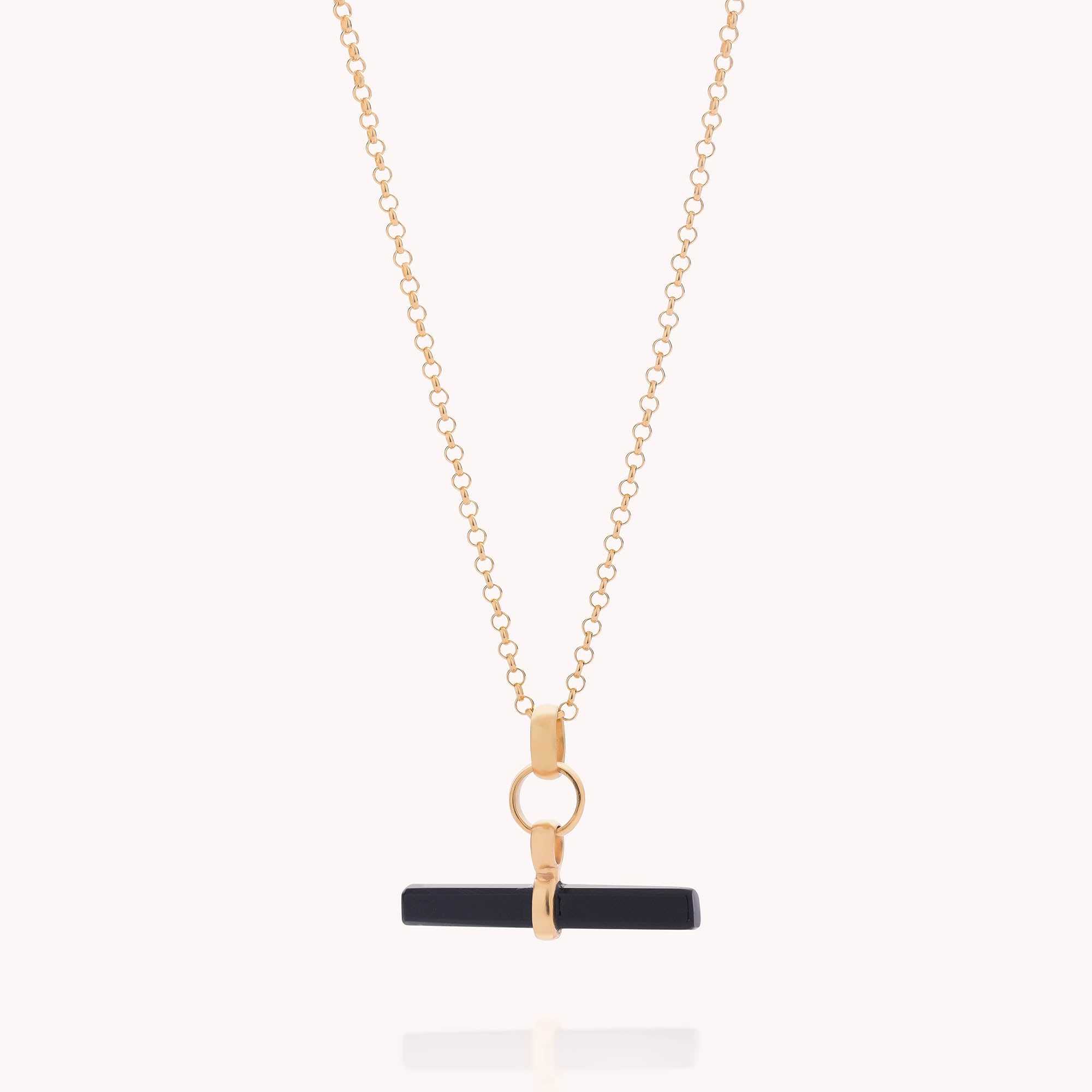 The Gemstone T Bar Necklace features a gold chain with a black T-bar pendant and gold circular accents, shown on a white background—a modern update to the classic gemstone necklace.
