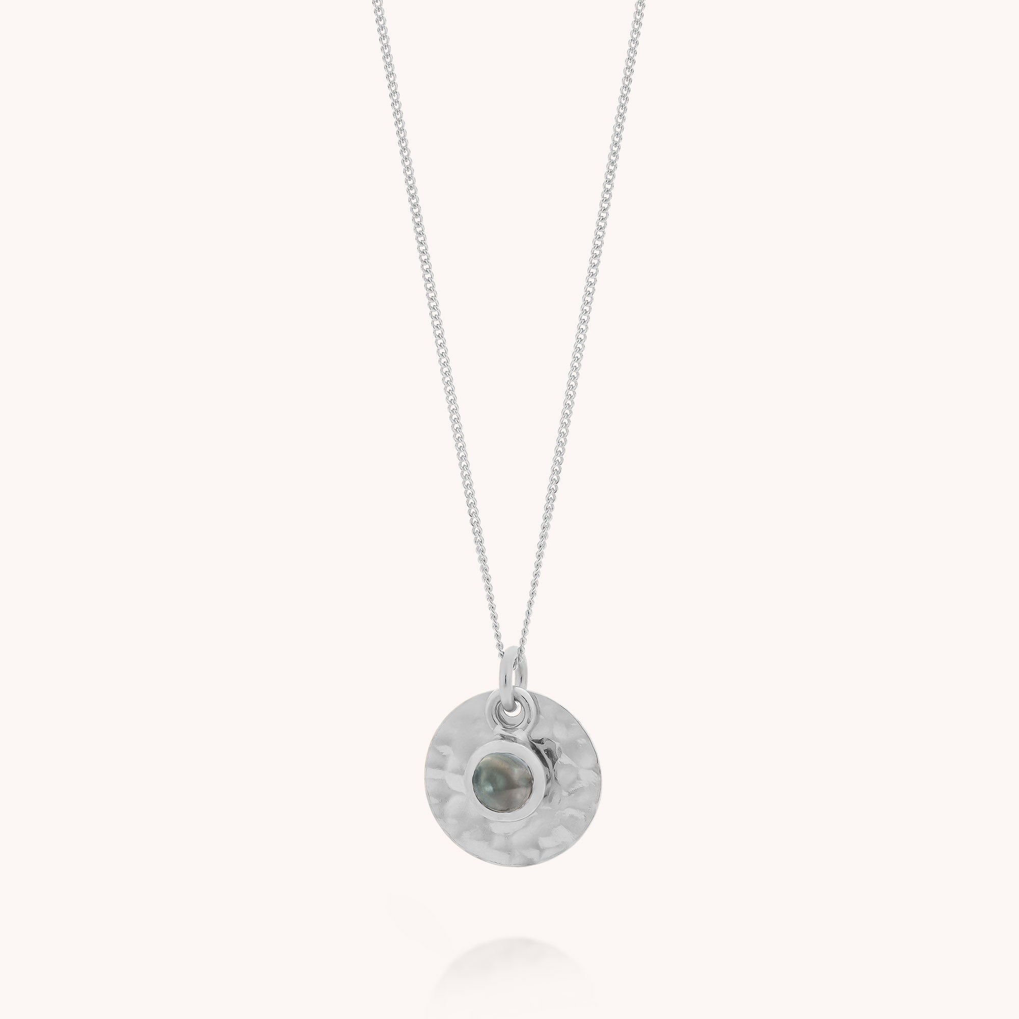 A delicate sterling silver Blue Topaz Luna Disc Necklace featuring a round, hammered pendant with a small, bezel-set blue topaz gemstone at the center—an elegant piece reminiscent of a December birthstone design.