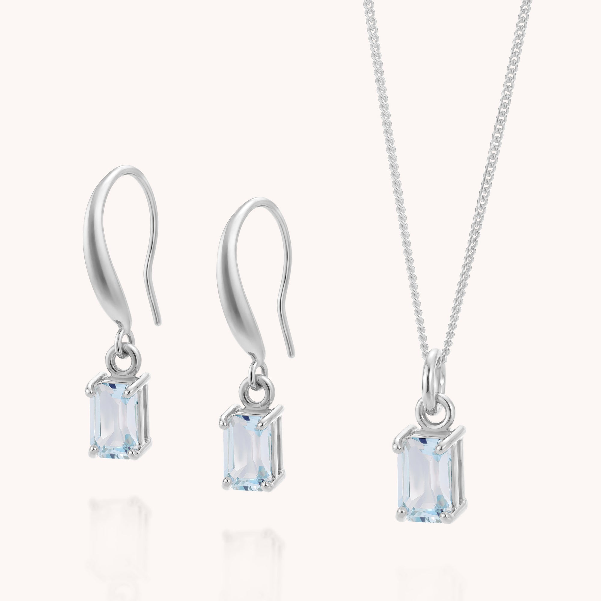 Introducing the Blue Topaz Octavia Necklace &amp; Earrings Set: an elegant jewellery ensemble featuring a pair of drop earrings and a sterling silver necklace, each showcasing a rectangular, light blue blue topaz gemstone in a timeless four-prong setting. This exquisite set is the perfect gift for someone special and offers a stunning way to celebrate December’s birthstone.