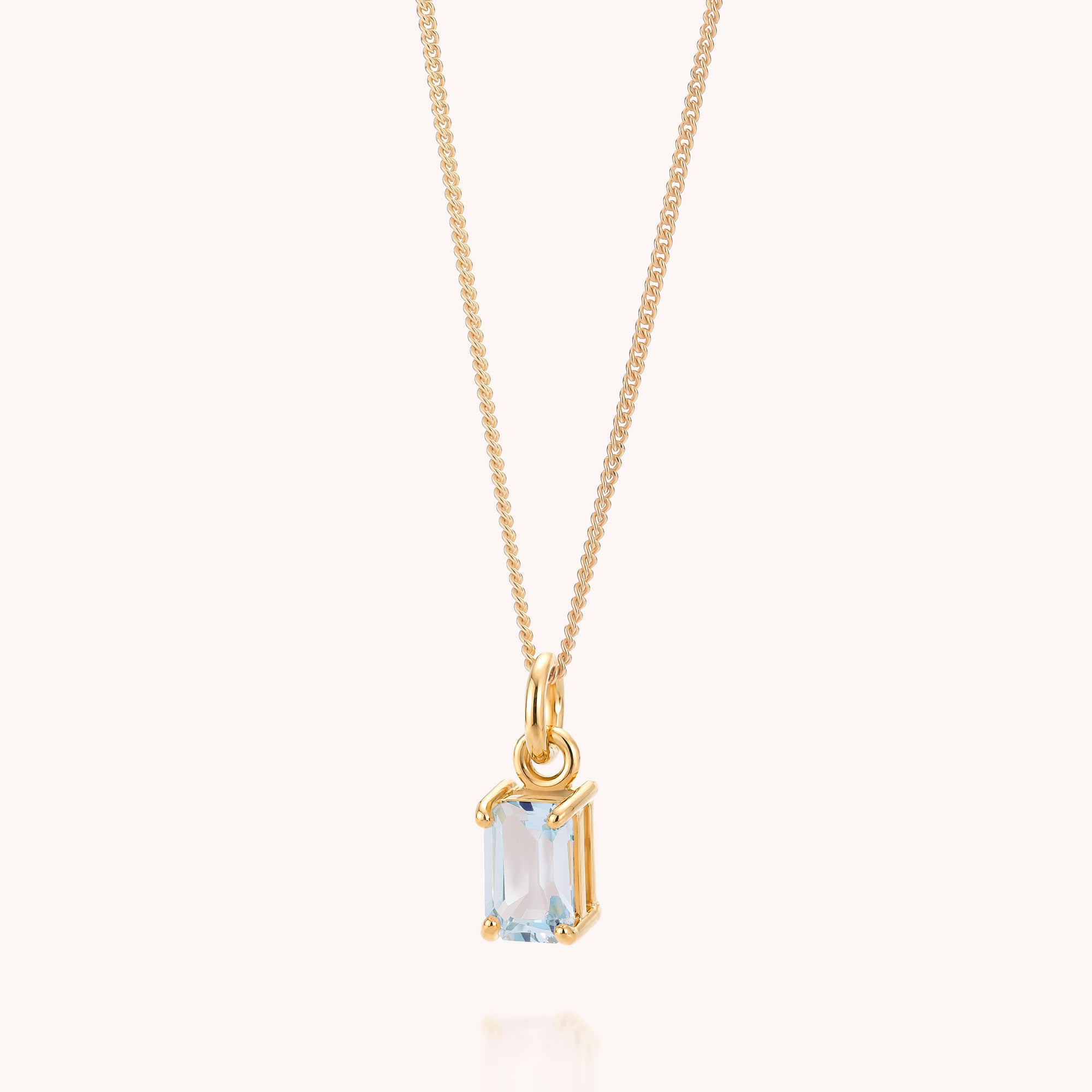 The Blue Topaz Octavia Necklace showcases a fine gold chain with a rectangular, light blue topaz gemstone pendant elegantly set in gold, highlighting the December birthstone. The necklace is photographed on a plain, light background.