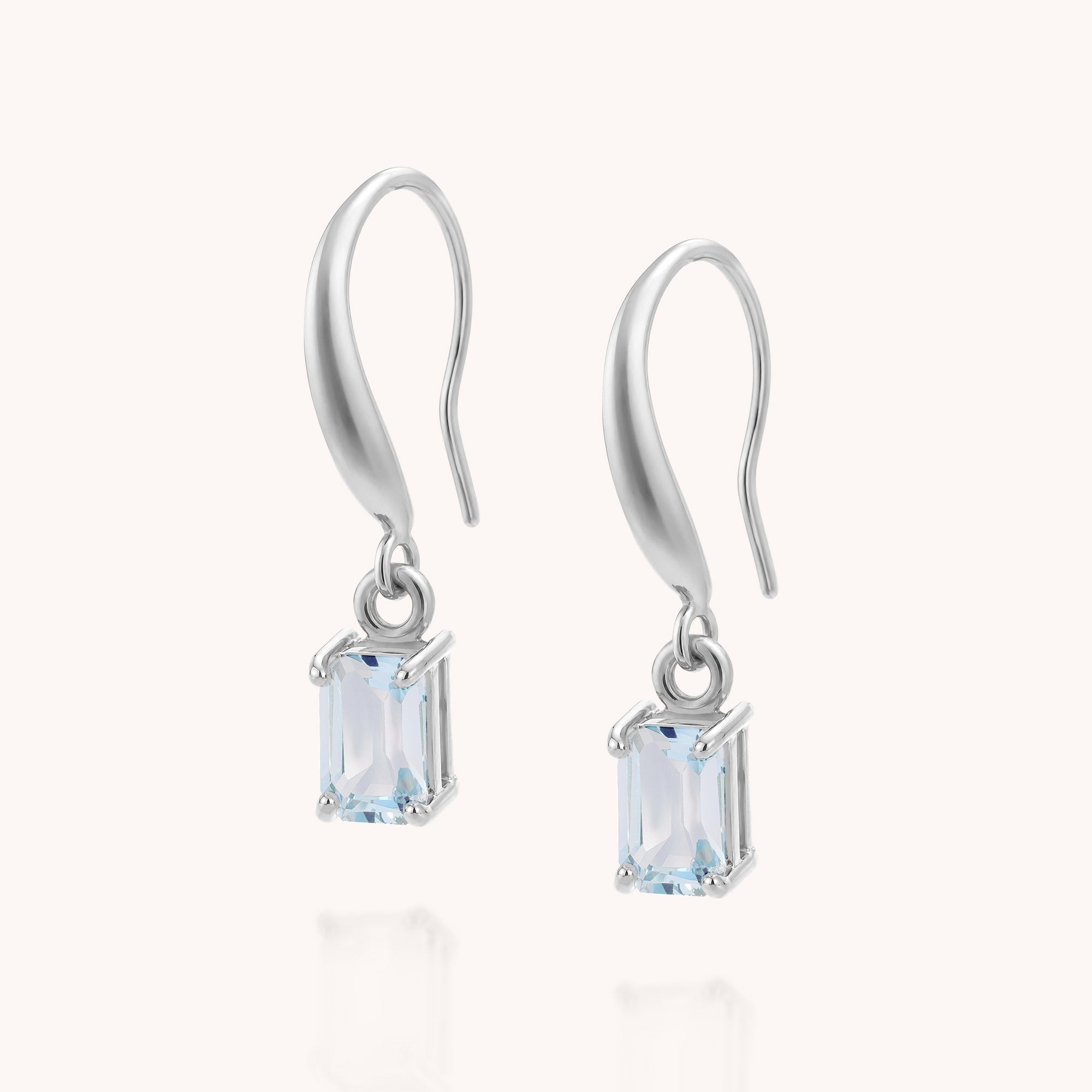 Introducing the Blue Topaz Octavia Drop Earrings—a pair of sterling silver drop earrings showcasing rectangular, light blue blue topaz gemstones reminiscent of December birthstones. Each gemstone is securely held in four-prong settings and elegantly presented against a white background.