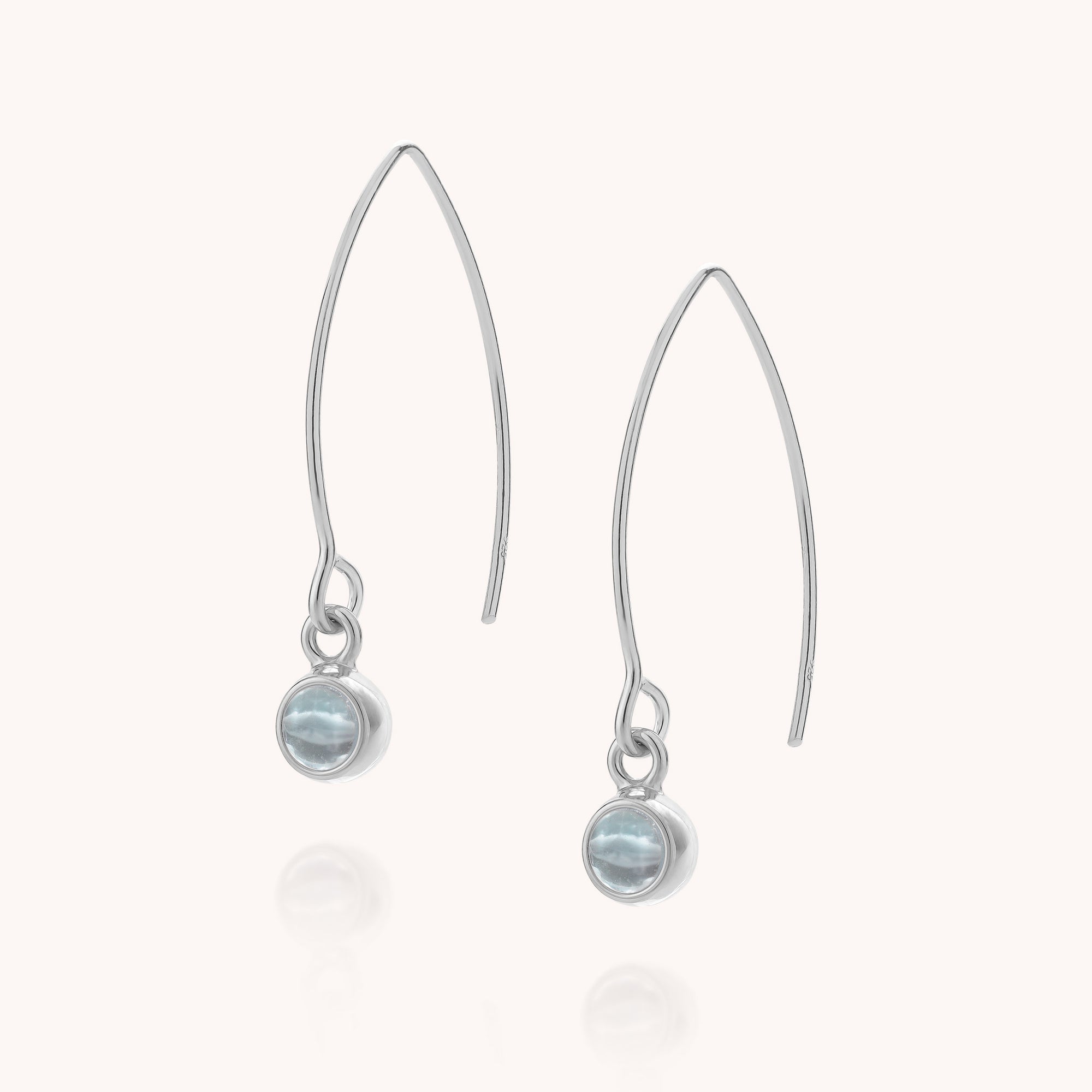 A pair of Blue Topaz Gem Dot Arc Earrings, each featuring a round, light blue topaz bezel-set at the base of silver hooks, displayed on a plain white background.