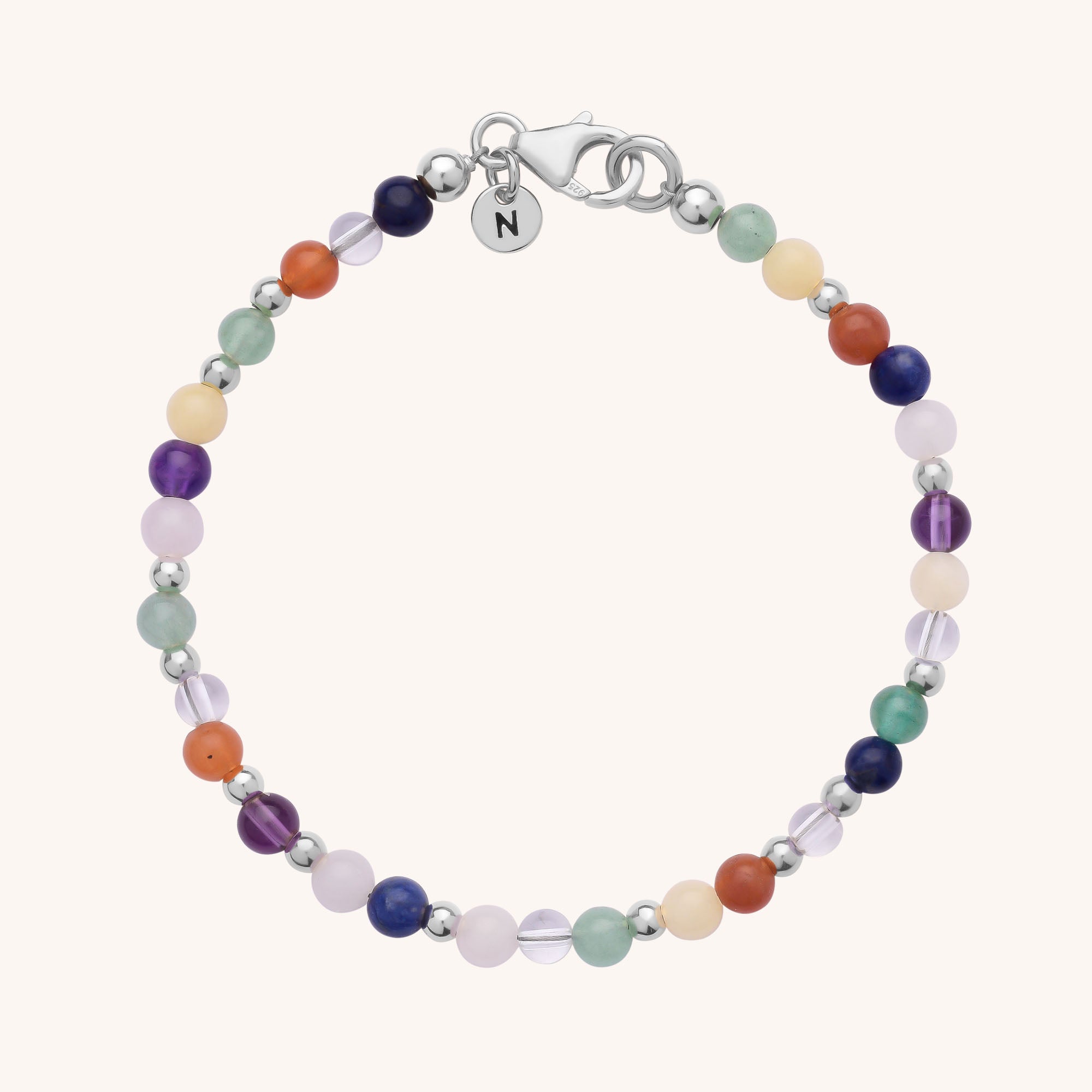 The Jewel Bead Chakra Bracelet features small, round multicolored natural gemstones and silver-toned beads, a lobster clasp, and a round N-engraved charm. Its vibrant beads symbolize the seven chakra colors.
