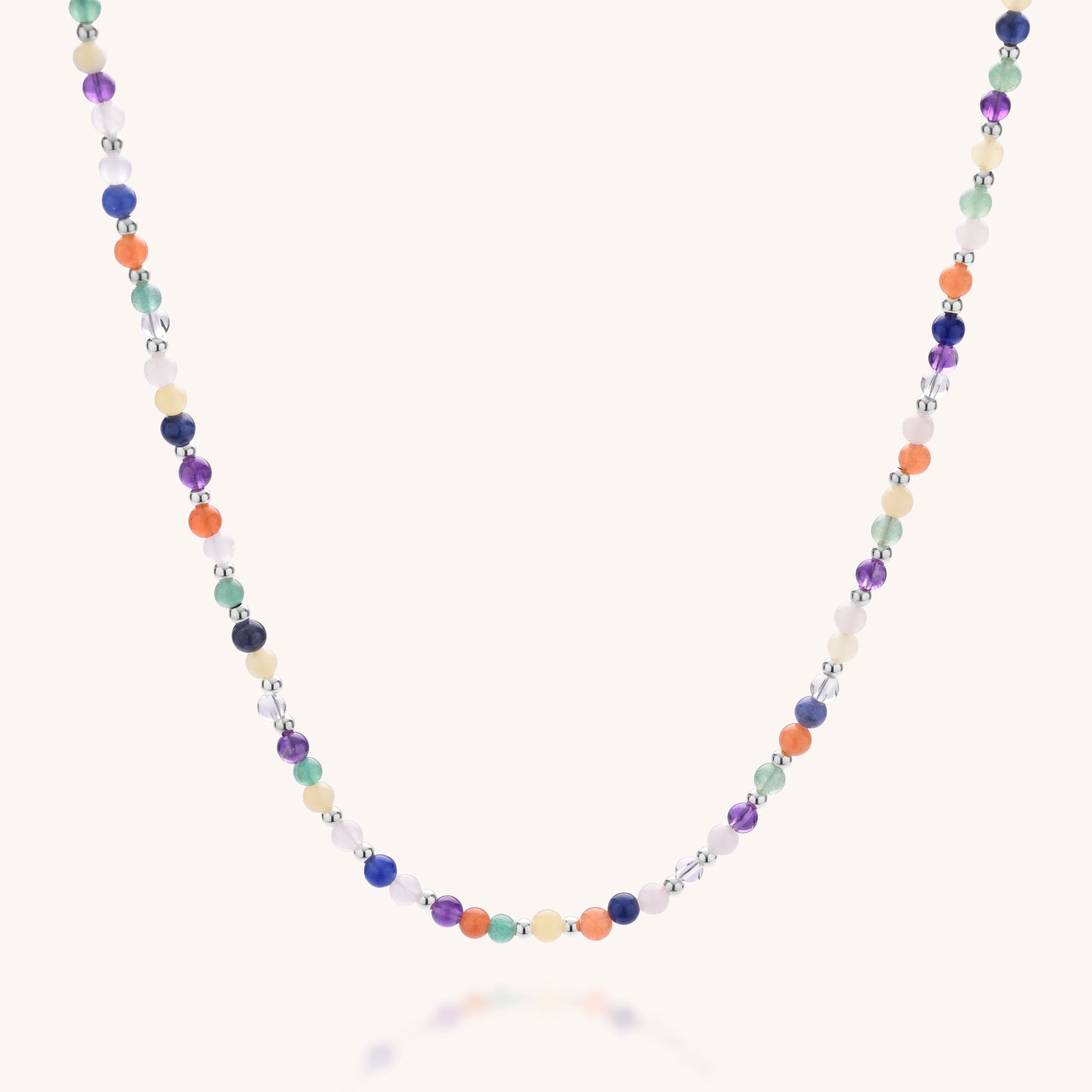 The Jewel Bead Chakra Necklace features small, natural gemstones in blue, orange, green, purple, white, and clear—each bead evenly spaced on a thin strand for a delicate look.