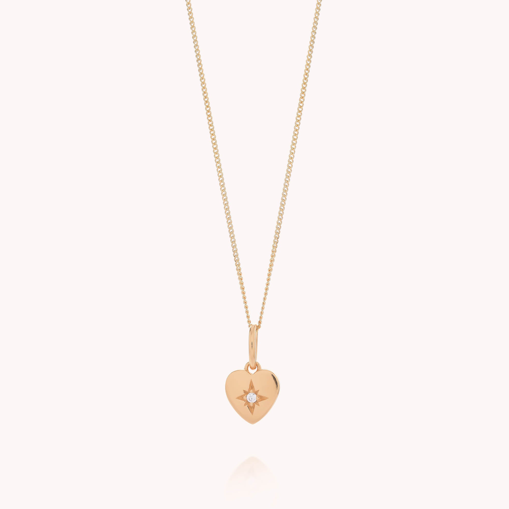 Introducing the Wish Heart Necklace: crafted from eco sterling silver with a radiant gold finish, this delicate necklace features a fine gold chain and a small, heart-shaped pendant adorned with a single sparkling diamond at its center. The elegant heart pendant is showcased against a softly hued, light background.