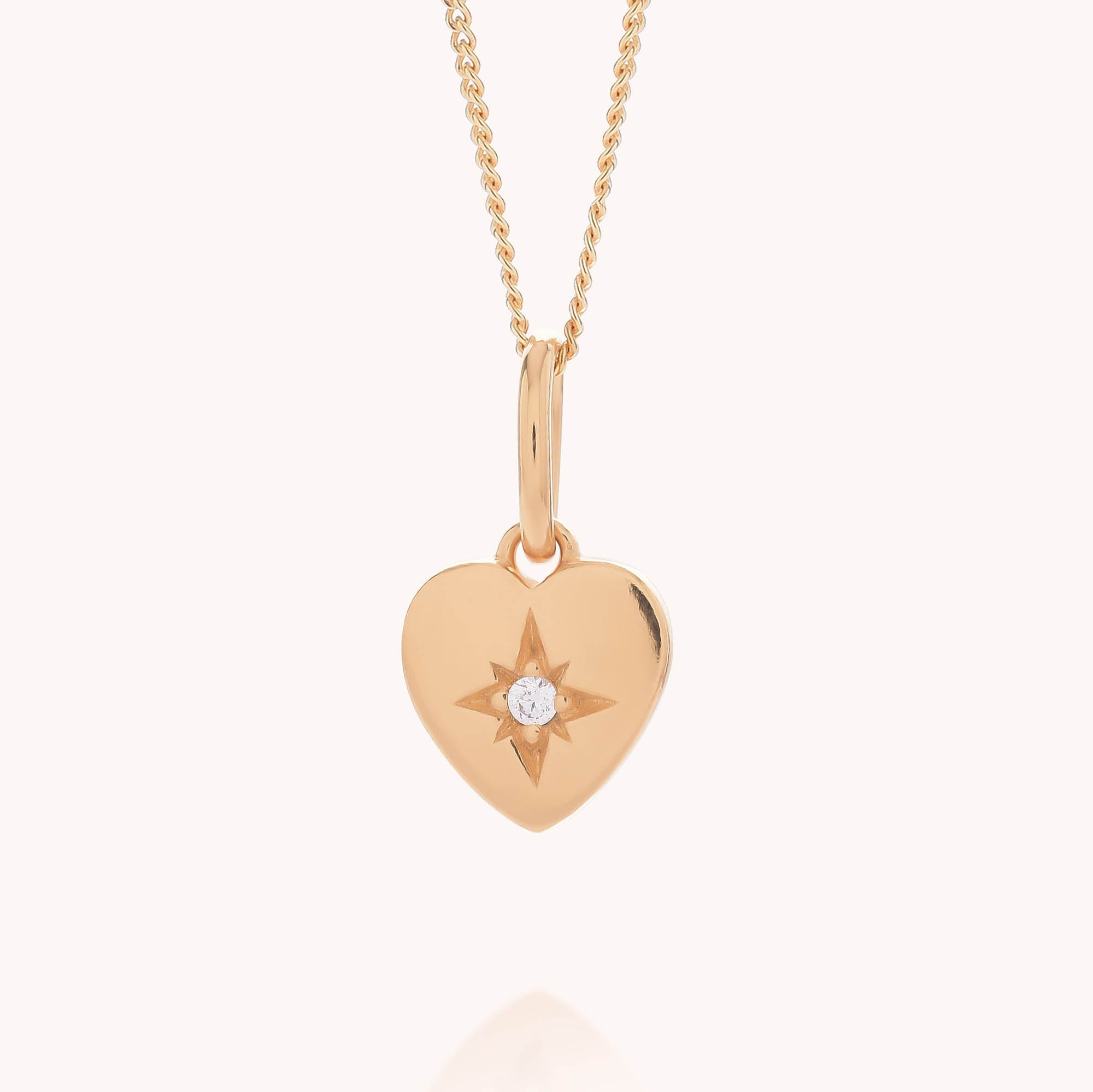 The Wish Heart Necklace features a gold heart-shaped pendant adorned with a star design and a central gemstone, elegantly suspended from a gold chain and beautifully showcased against a light background.