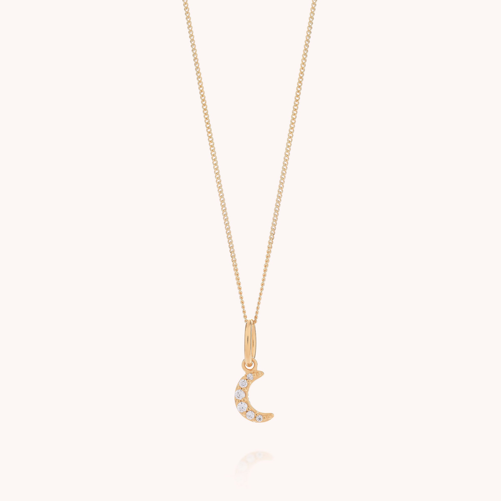 The Starlit Moon Necklace is a delicate gold chain necklace featuring a small crescent moon pendant embellished with sparkling white gemstones, displayed against a simple light background.