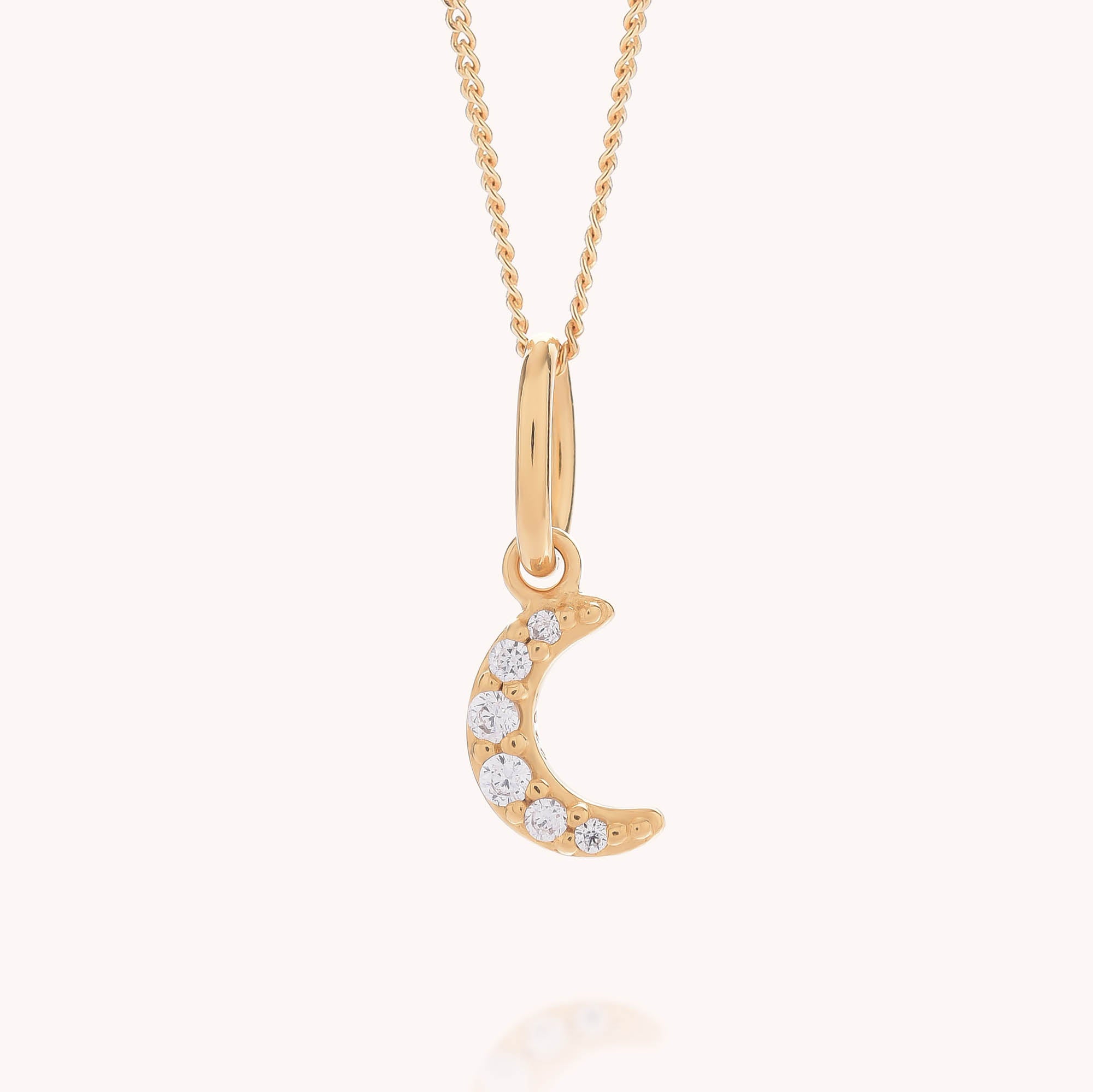 Introducing the Starlit Moon Necklace: crafted in eco sterling silver and plated with gold, this elegant necklace showcases a graceful crescent moon pendant set with six shimmering clear gemstones. Suspended on a delicate chain and photographed against a light background, the Starlit Moon Necklace radiates celestial charm with timeless appeal.