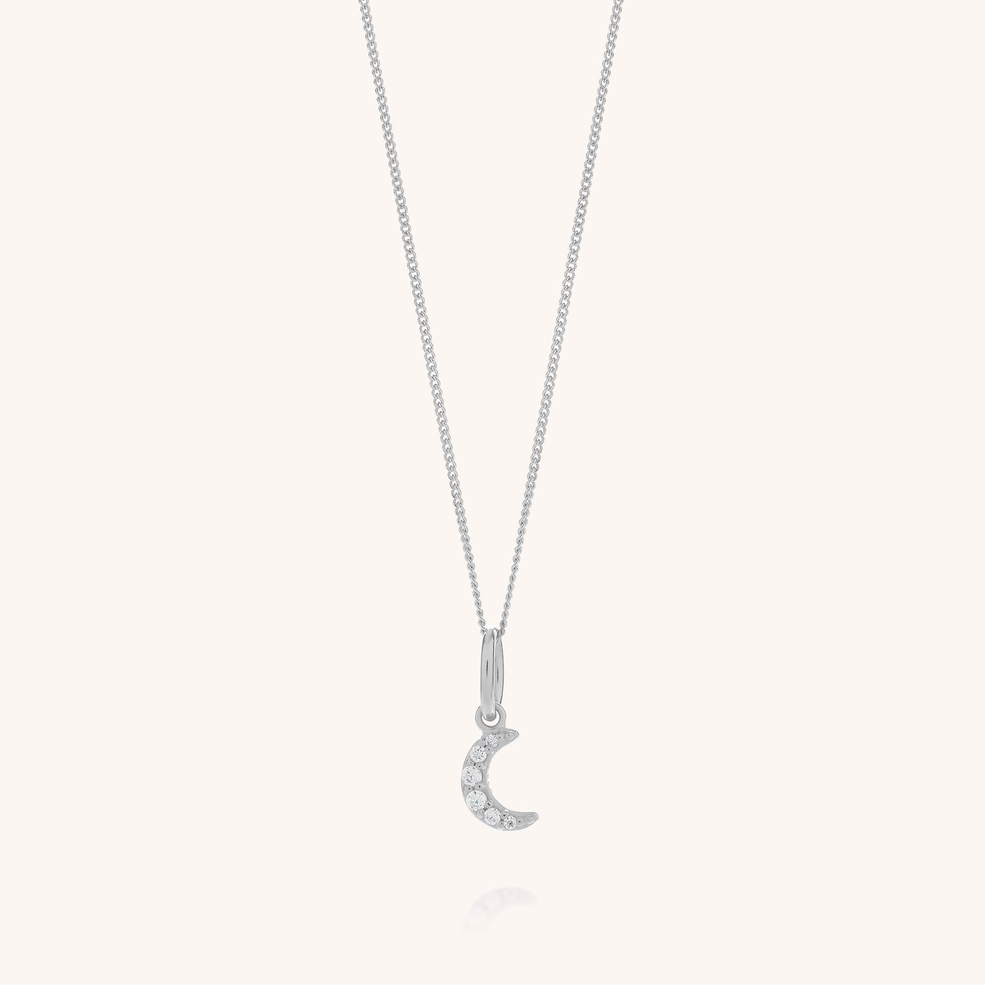 The Starlit Moon Necklace is crafted from eco sterling silver and features a petite crescent moon pendant embellished with sparkling clear gemstones, showcased against a simple light background.