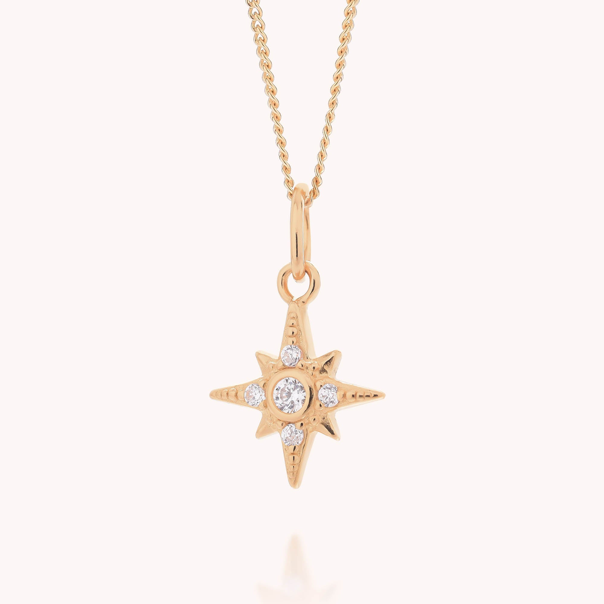 The Celestial Star Necklace features an eight-pointed, star-shaped pendant adorned with small cubic zirconia accents, suspended from a simple gold chain and showcased against a light background.
