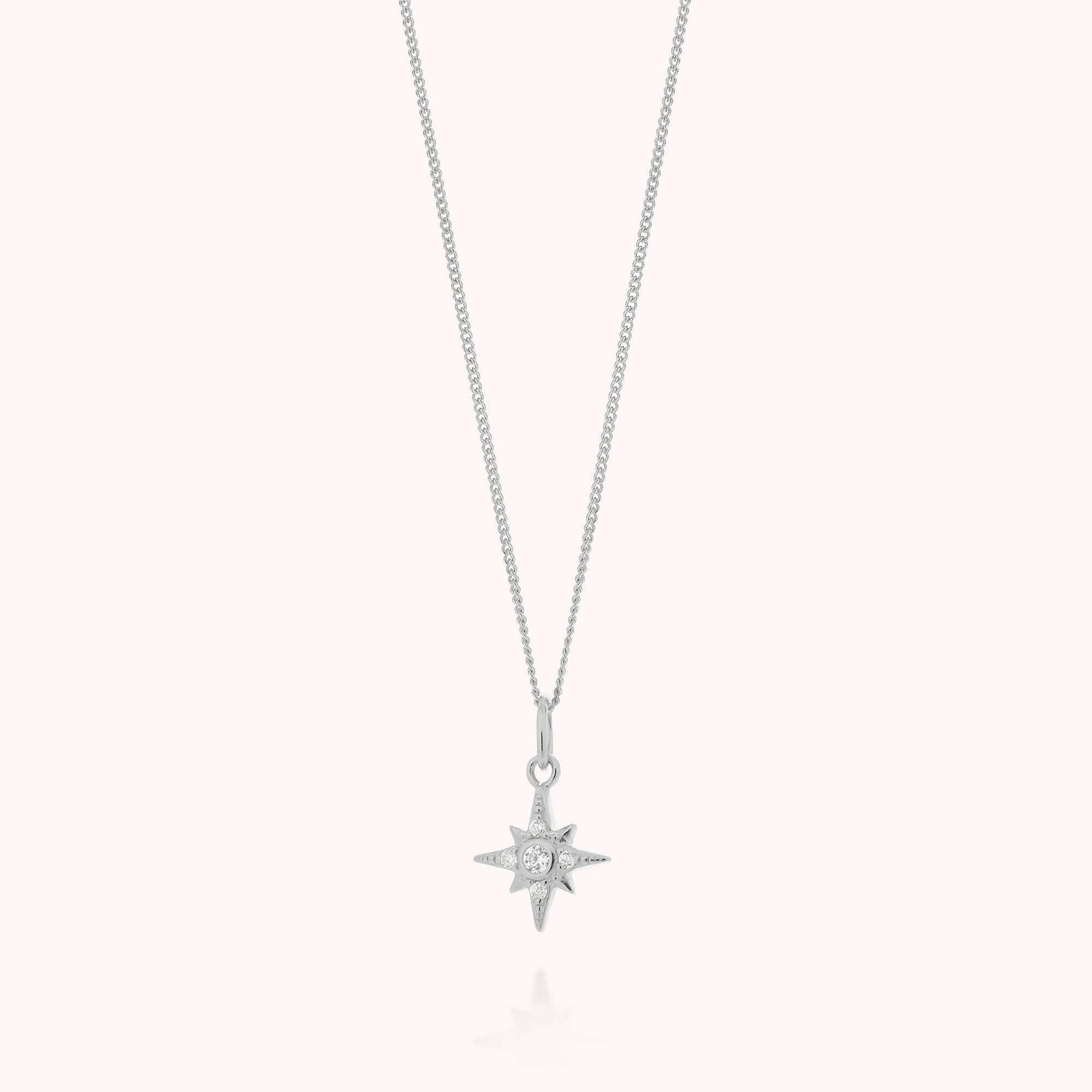The Celestial Star Necklace features a delicate silver chain with a star-shaped pendant, accented by a small central cubic zirconia gemstone. The background is plain and light-colored.