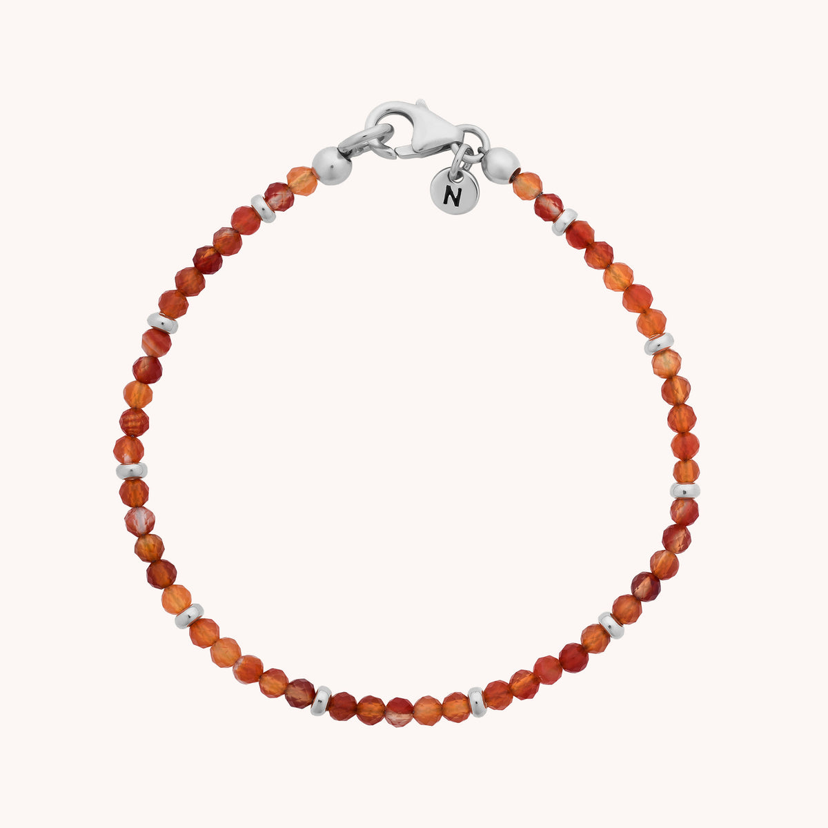 Delicate handcrafted jewellery featuring the Carnelian Orbit Bracelet - July, adorned with small, faceted orange carnelian beads, silver accents, a silver lobster clasp, and finished with a round charm engraved with the letter N.