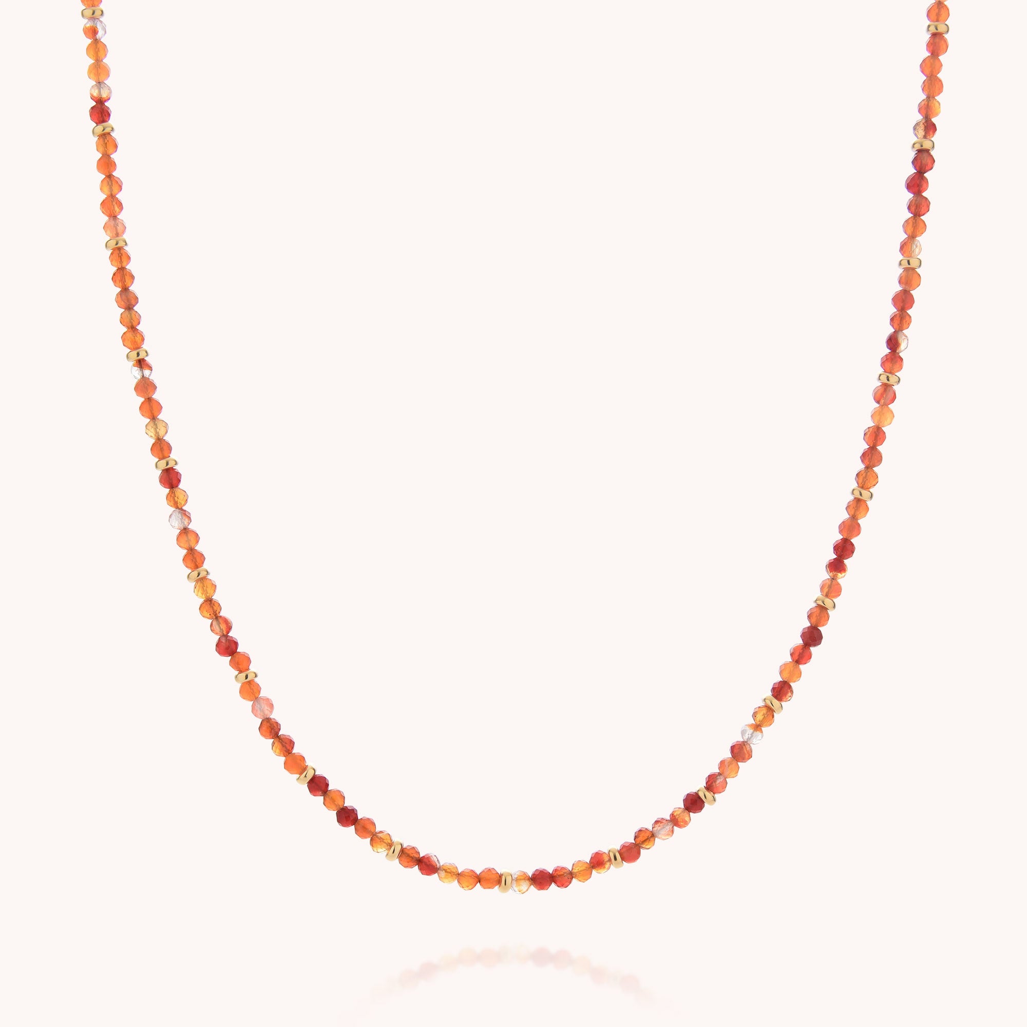 The Carnelian July Birthstone Orbit Necklace showcases delicate, small round carnelian beads in a spectrum of orange, red, and gold hues, evenly arranged along a fine string. Presented on a plain light background, this elegant gemstone jewelry piece is perfect for adding warmth and color to any outfit.