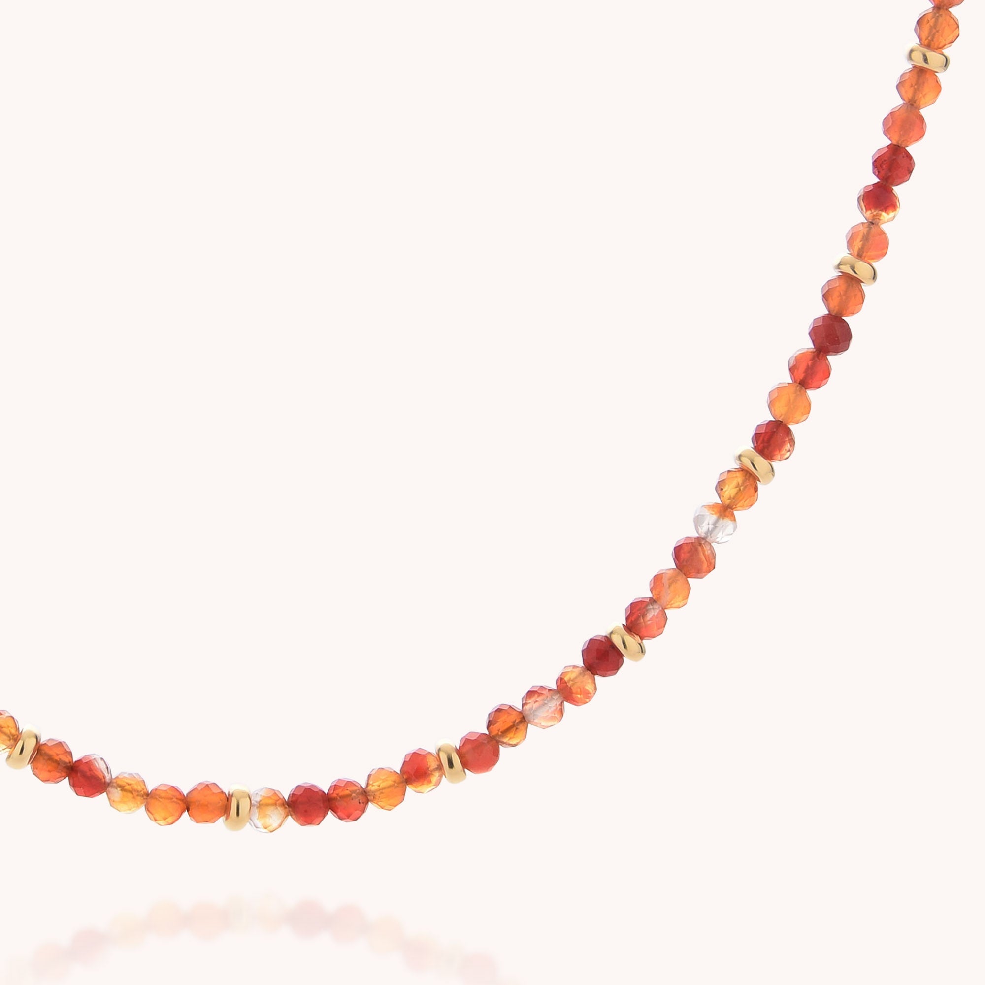 Introducing the Carnelian July Birthstone Orbit Necklace—a delicate piece adorned with small round beads in vibrant shades of red, orange, and gold. Arranged gracefully in a gentle curve against a light background, this necklace is ideal for those who love gemstone jewelry or are looking for a distinctive July birthstone accessory.