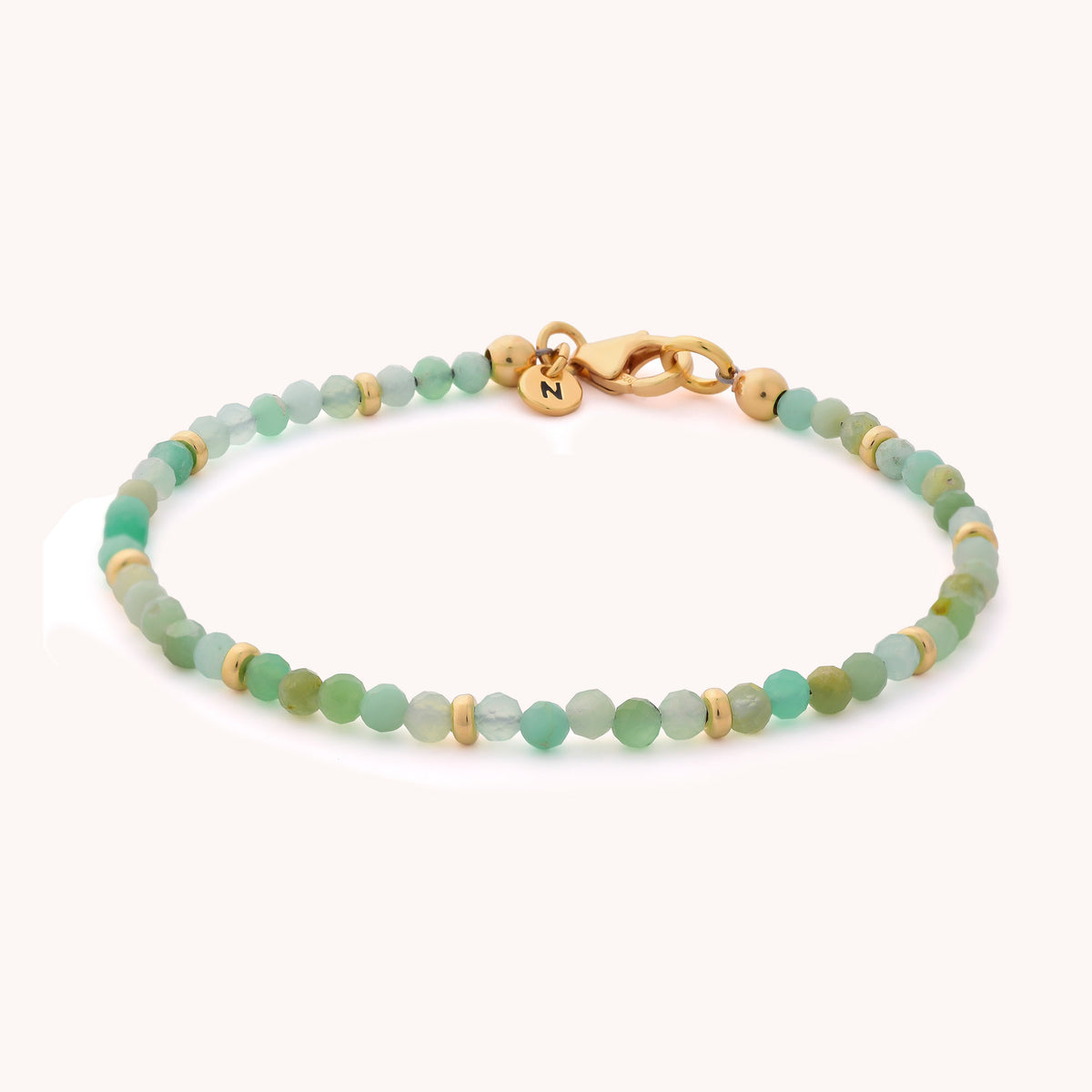 Introducing the Chrysoprase Orbit Bracelet - May: a handcrafted piece adorned with delicate green chrysoprase beads—the May birthstone—accented by gold spacers and a gold clasp. A tiny round charm, engraved with the letter N, adds a personal touch to this elegant and meaningful gemstone bracelet.