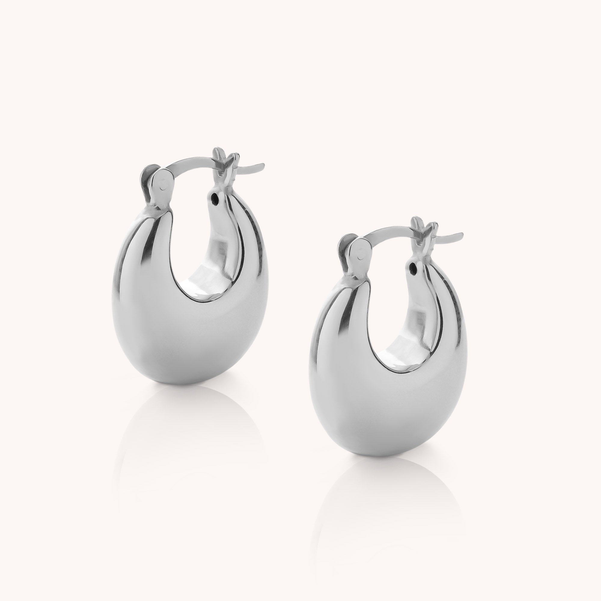 A pair of Dome Hoop Earrings in shiny silver, featuring a smooth, rounded design and secure latch-back closures, displayed against a simple light background—ideal sculptural earrings for everyday wear.
