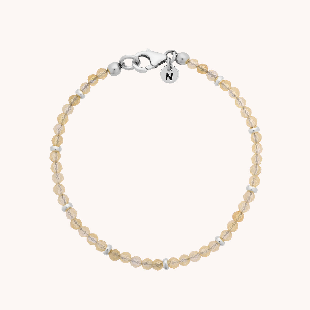 Introducing the Citrine Orbit Bracelet - November: an elegant piece adorned with small, round, light brown citrine beads and silver spacers, finished with a silver lobster clasp and a dainty round charm engraved with the letter N—perfect as a birthstone accessory for November.