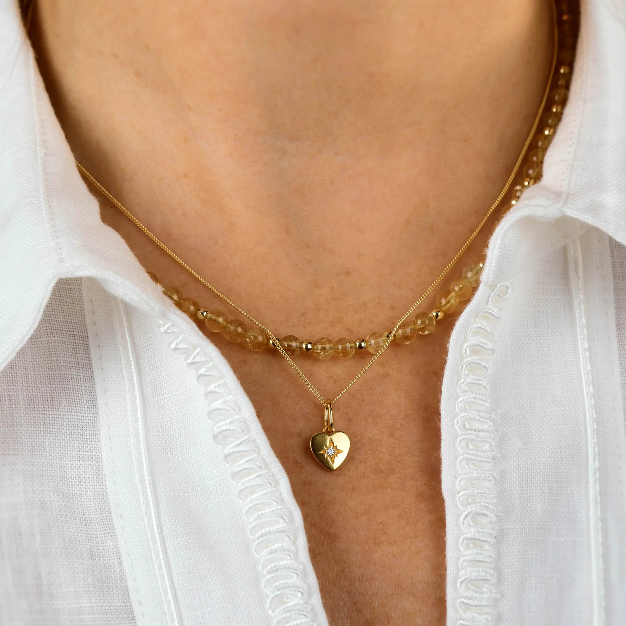 A person wearing a white shirt has two necklaces: a beaded choker and the Wish Heart Necklace, which features an eco sterling silver heart pendant adorned with a small star design.