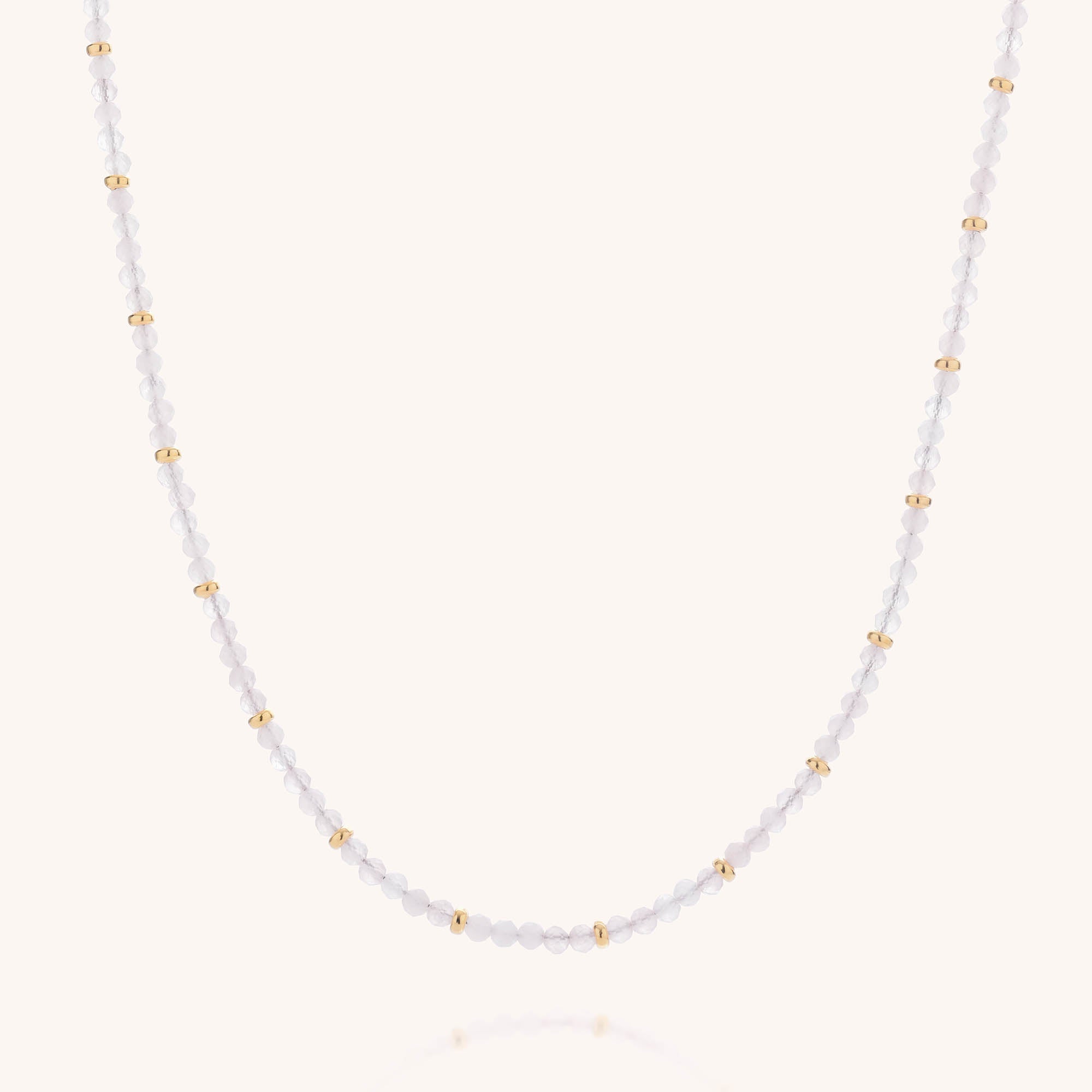 The Rose Quartz Orbit Necklace is a delicate piece featuring small white beads and evenly spaced gold beads, expertly crafted with gold-plated eco sterling silver and accented by faceted rose quartz beads, displayed against a plain light background.