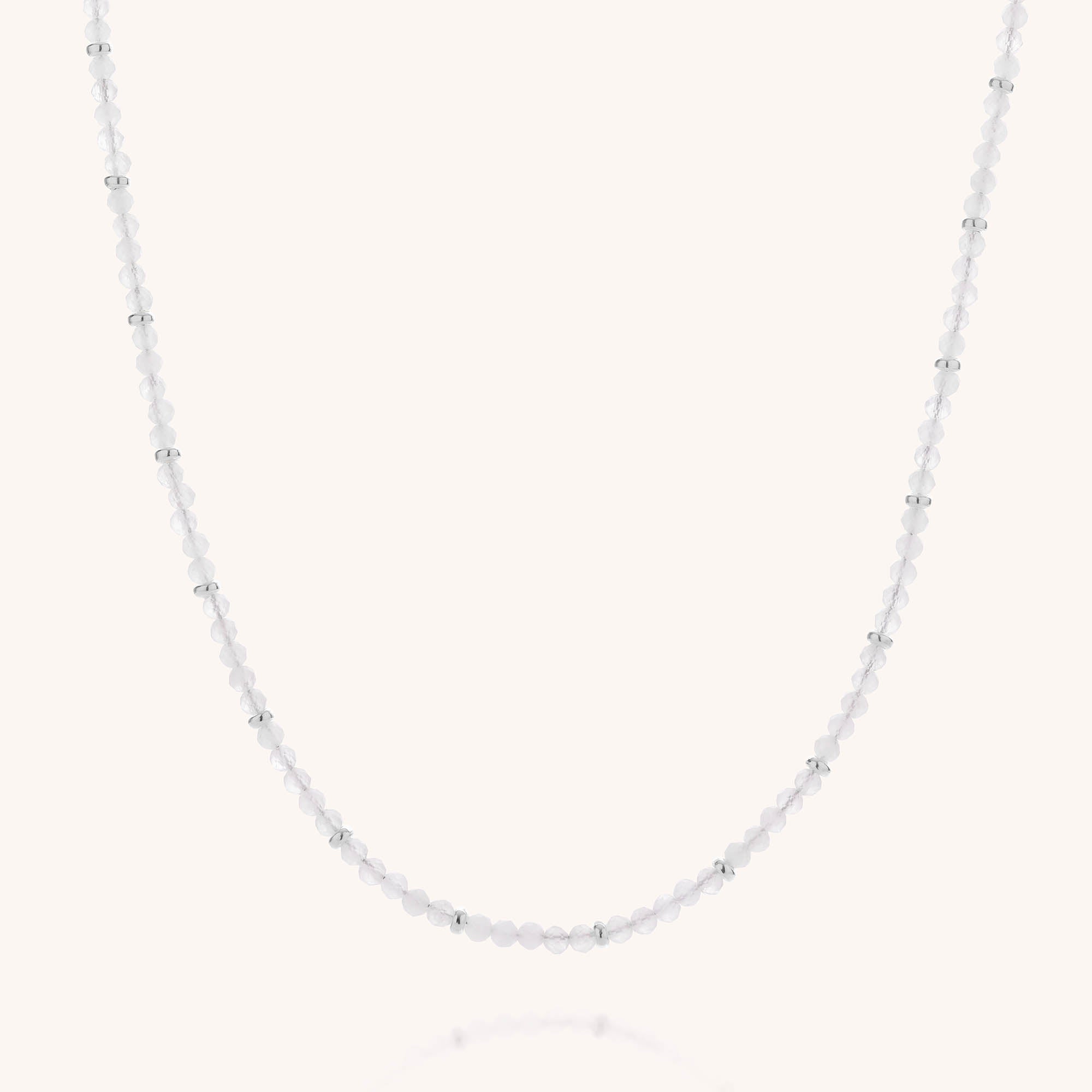 The Rose Quartz Orbit Necklace features small white beads and silver beads, accented with faceted rose quartz for a subtle hint of color, shown on a plain white background.