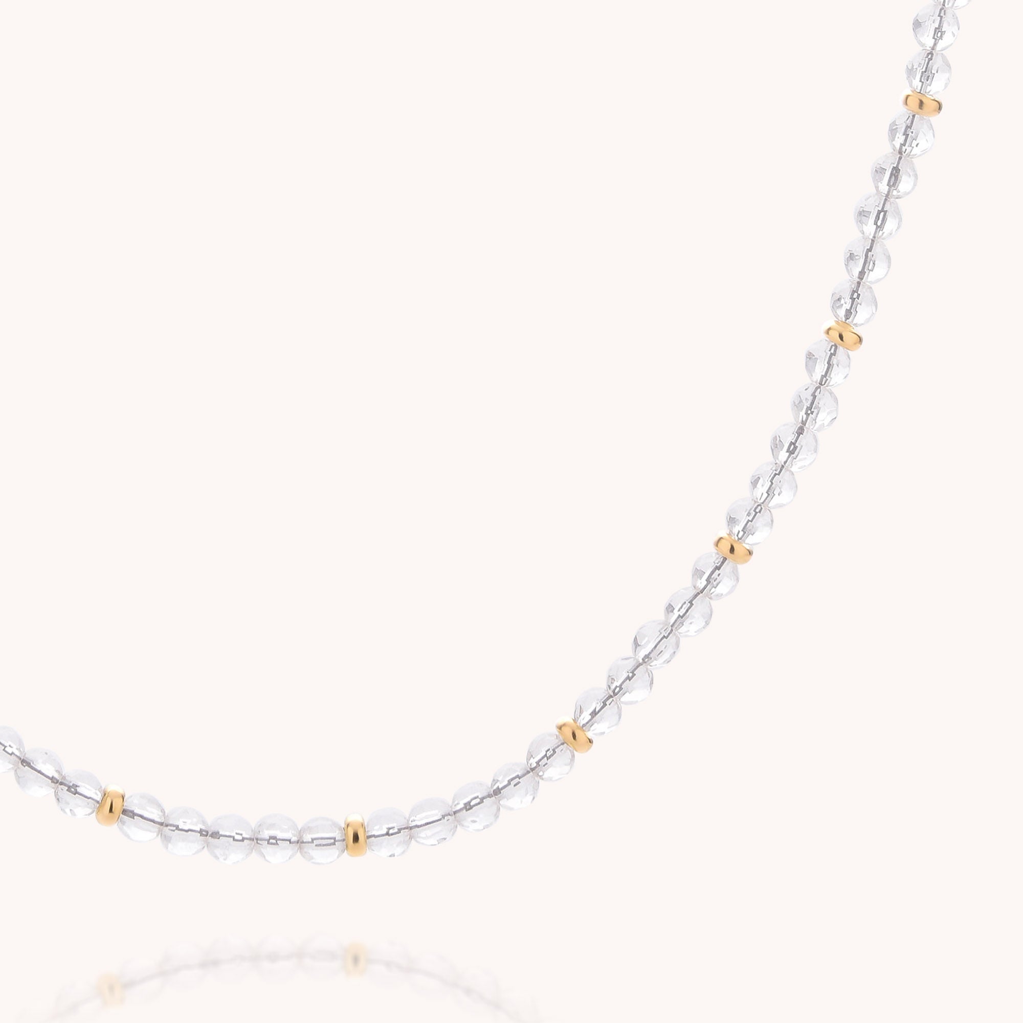 Introducing the Clear Quartz April Birthstone Orbit Necklace—a delicate piece featuring small, clear quartz round beads and evenly spaced gold spacer beads, elegantly displayed on a light background and inspired by the timeless beauty of the April birthstone.