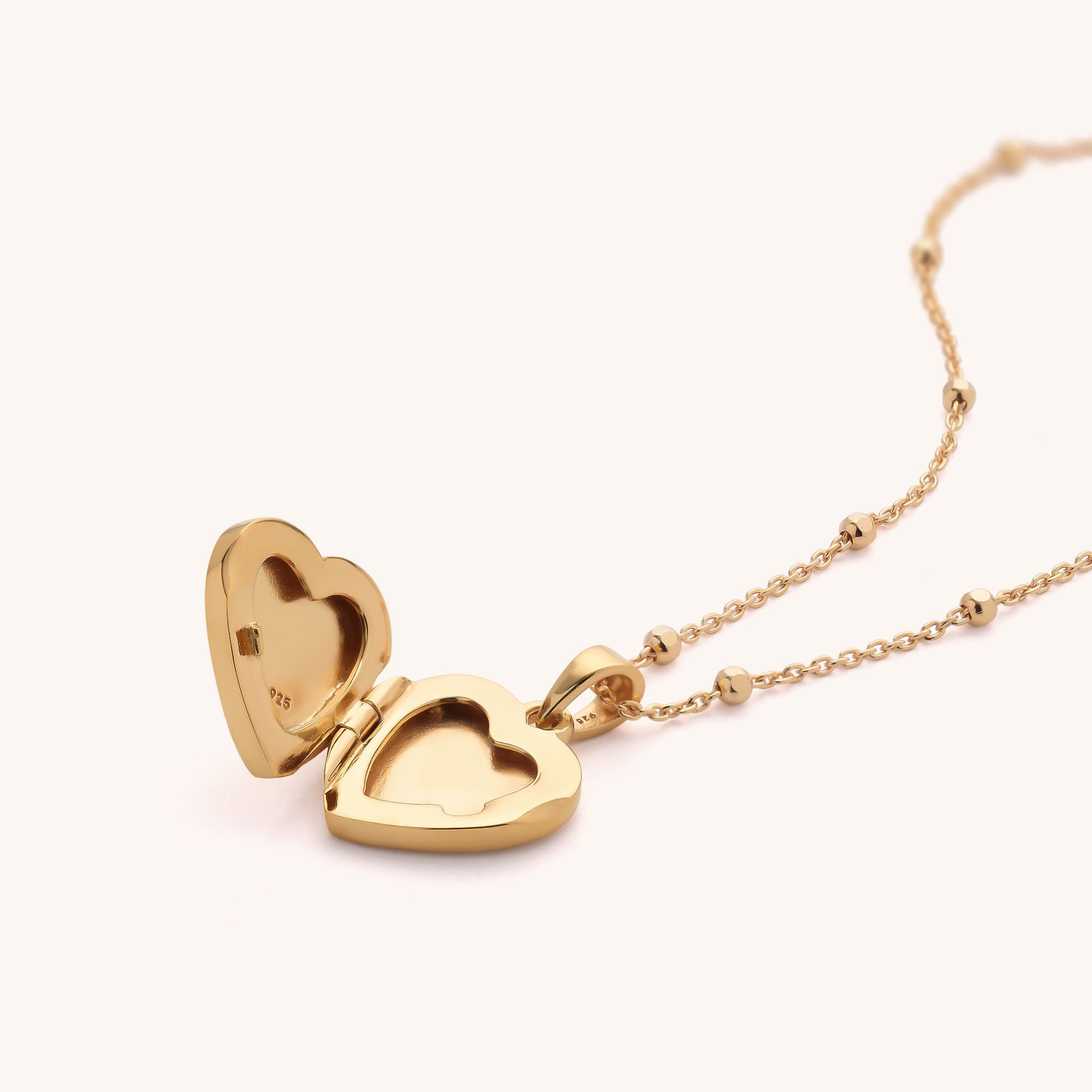 The Aura Heart Locket Necklace features a gold, heart-shaped pendant on a delicate chain. It opens to hold a small photo or keepsake, and its smooth, shiny surface beautifully catches the light.