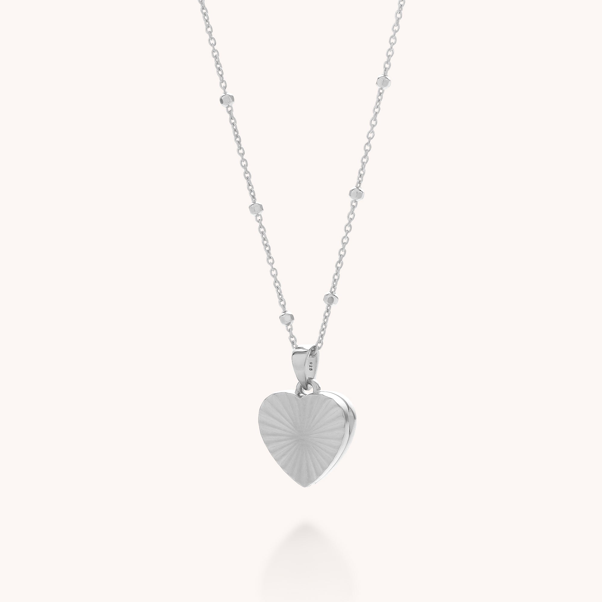 The Aura Heart Locket Necklace is a delicate sterling silver piece with a beaded chain and heart-shaped pendant, shown against a plain white background.