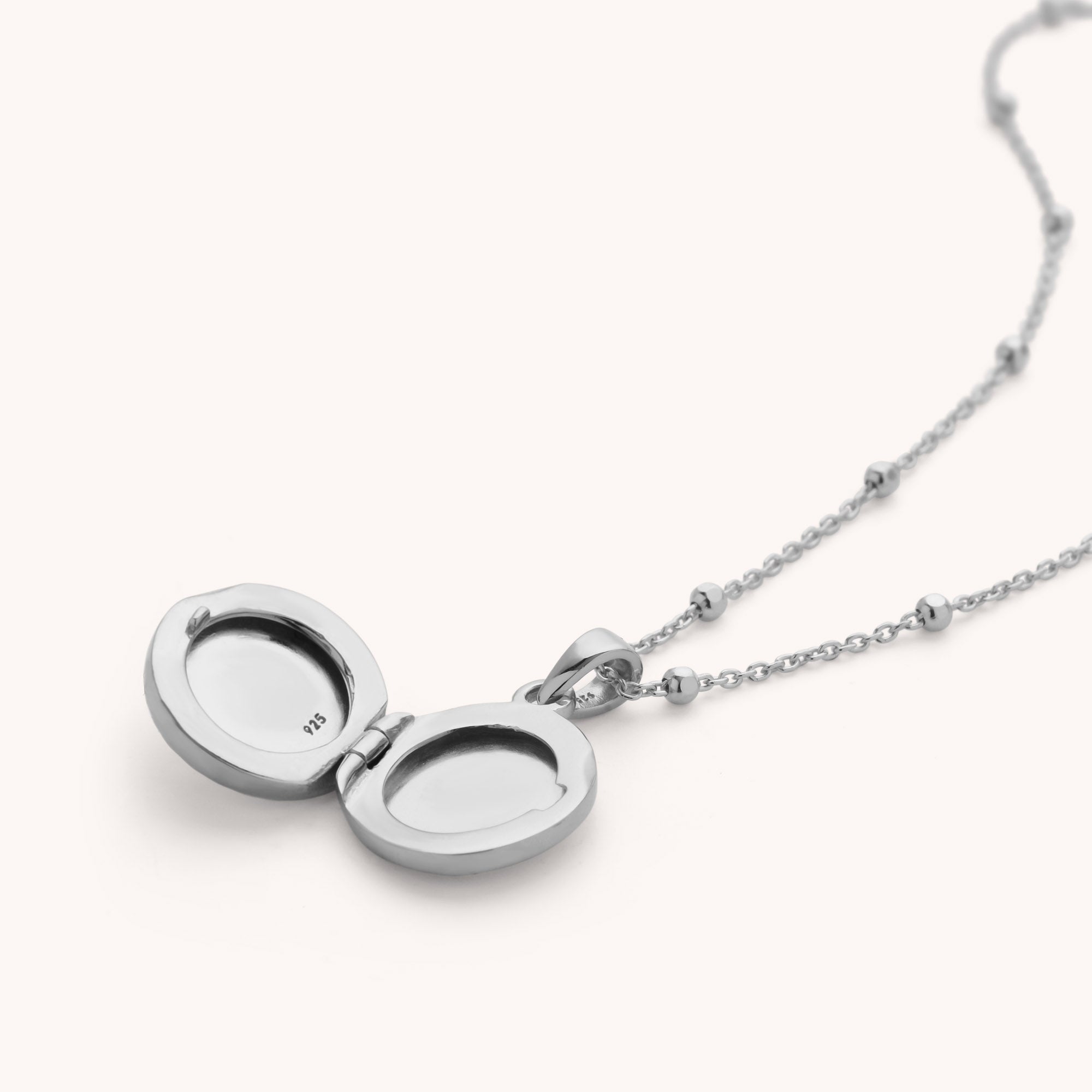 The Aura Round Locket Necklace features a sterling silver round pendant on a delicate chain, opening to reveal two spaces inside the locket for photos or cherished keepsakes.