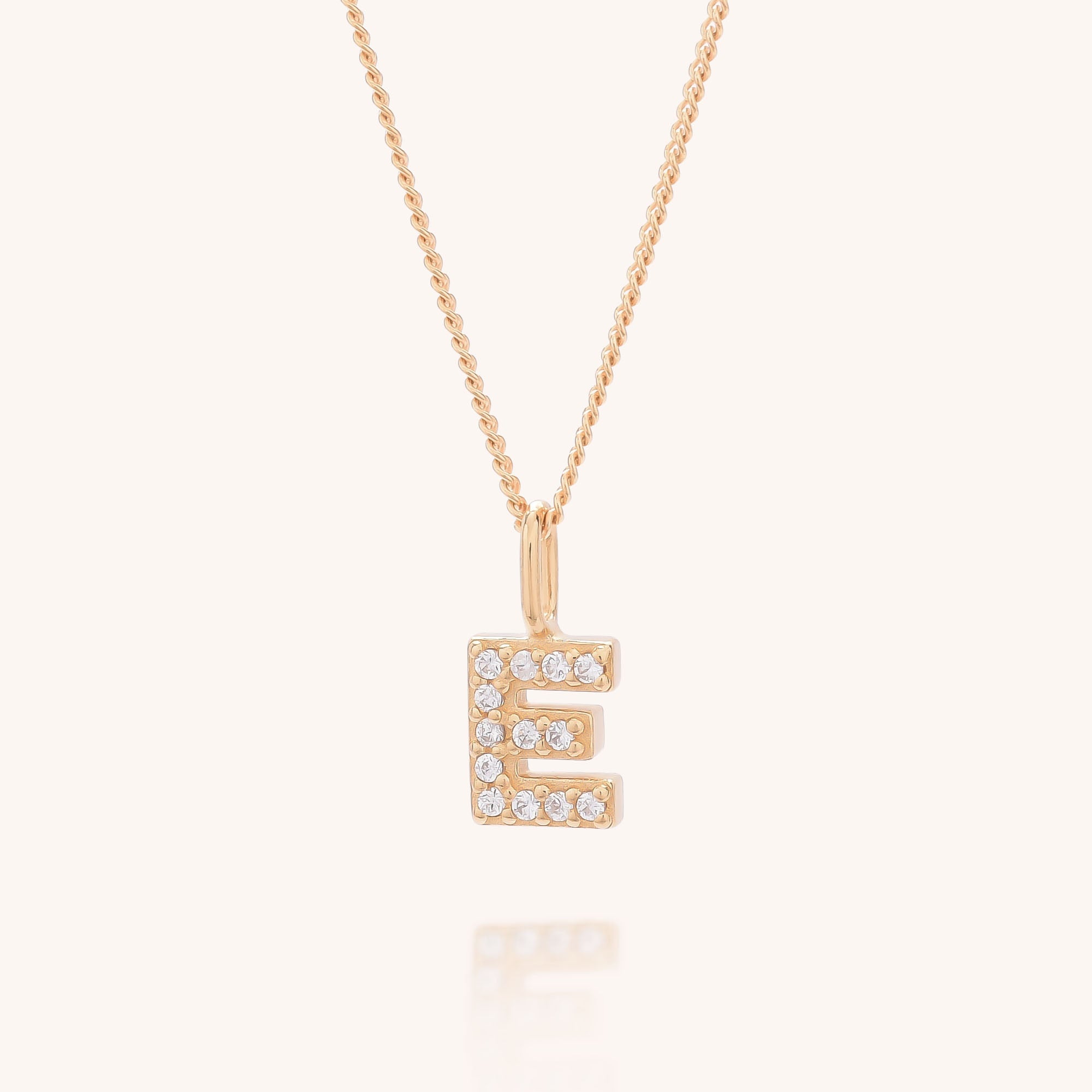 The Initial Sparkle Necklace features a gold pendant in the shape of the letter E, adorned with sparkling cubic zirconia stones, displayed on a simple light background.