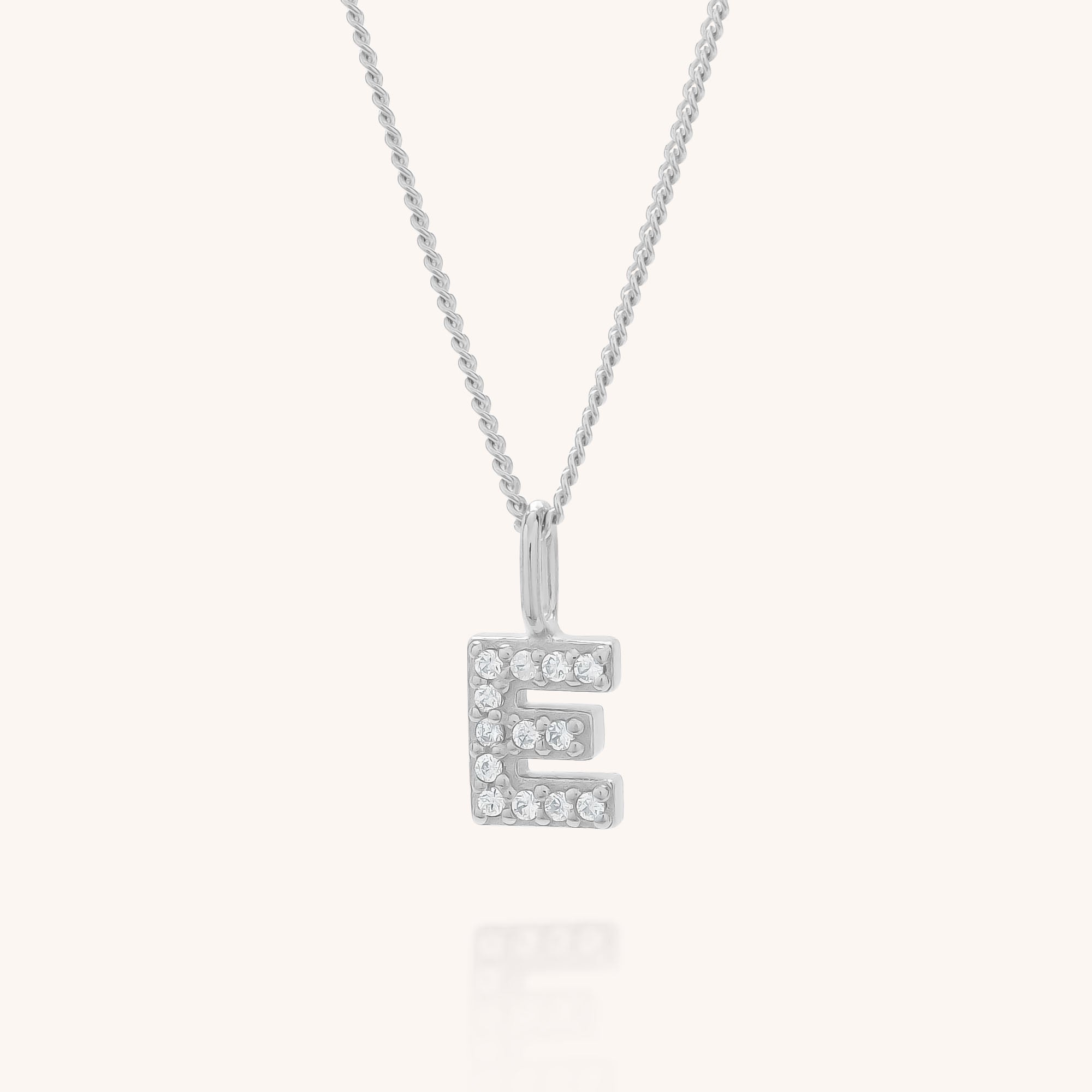 The Initial Sparkle Necklace features a silver pendant shaped like the letter E, adorned with sparkling cubic zirconia stones, shown against a plain light background.