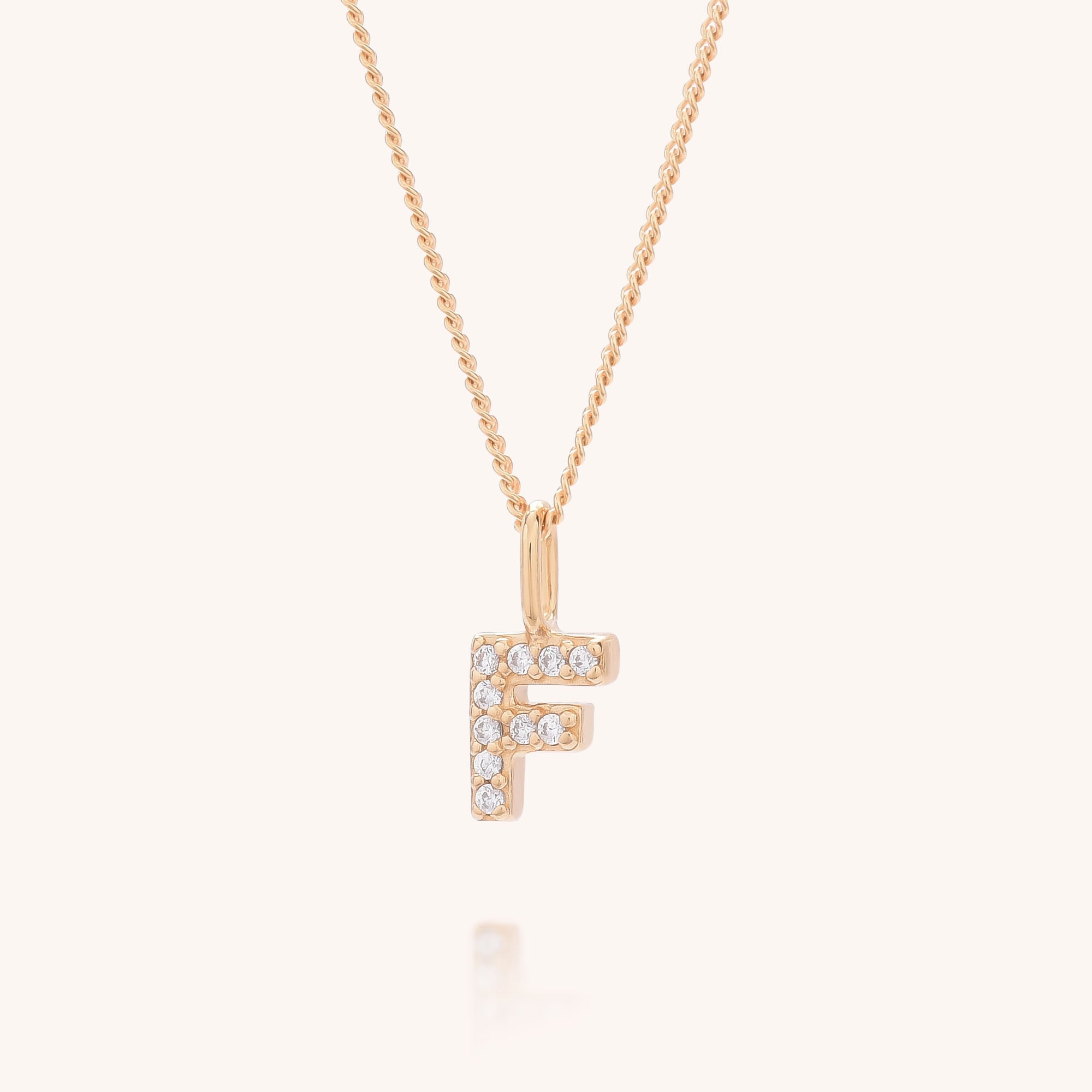The Initial Sparkle Necklace showcases a gold &#39;F&#39; pendant adorned with sparkling cubic zirconia, presented on a plain, light background.