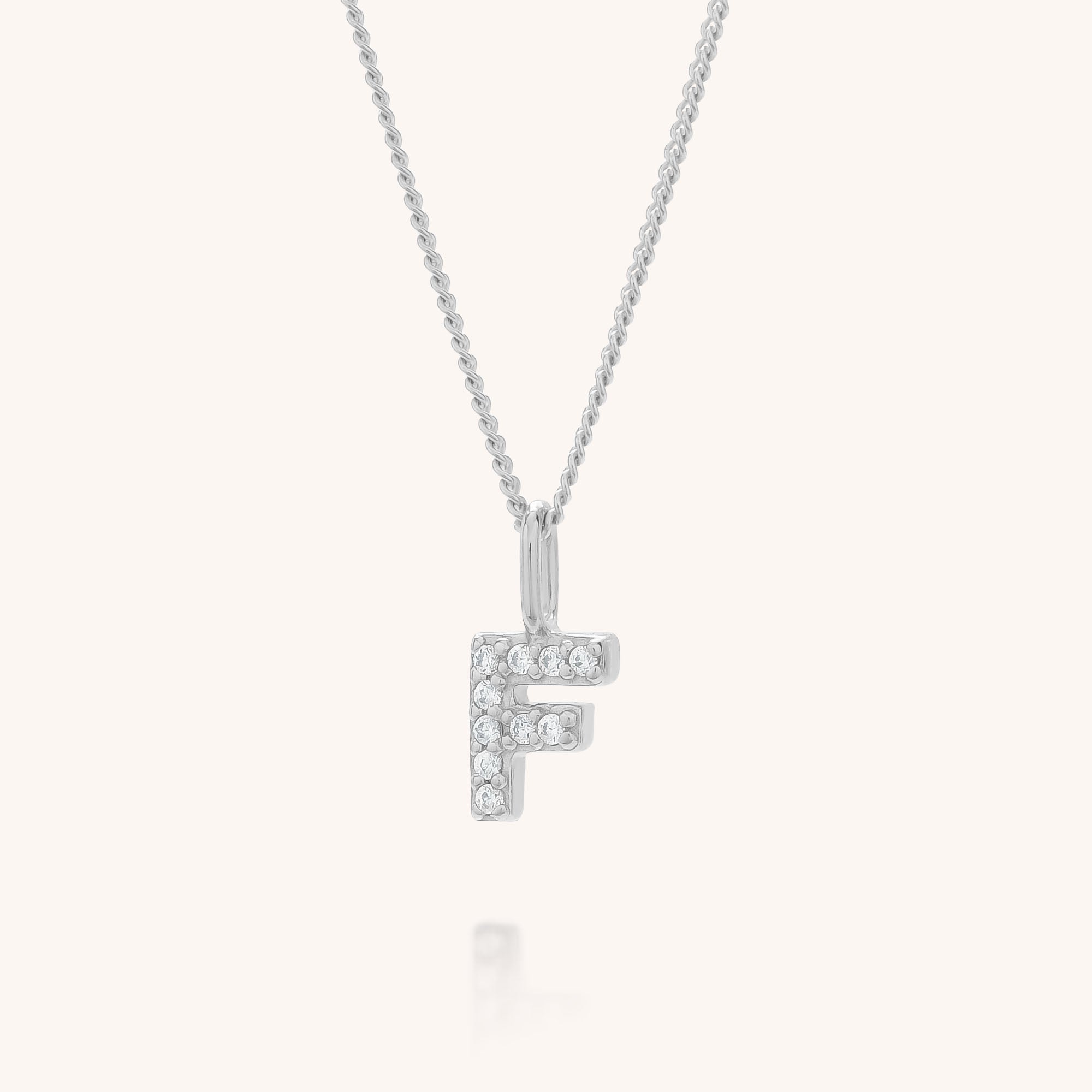 The Initial Sparkle Necklace is a silver personalised necklace with an F-shaped pendant adorned with sparkling cubic zirconia, hanging from a delicate chain against a plain, light background.