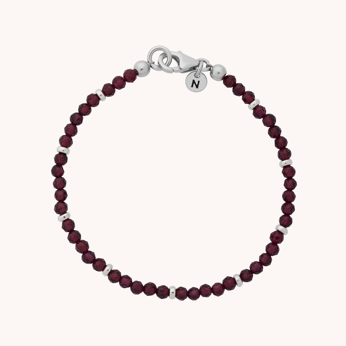 Introducing the Garnet Orbit Bracelet - January: a delicate accessory featuring small round burgundy garnet beads accented with sterling silver spacers, finished with a lobster clasp and a petite round charm engraved with the letter “N.” This beautiful bracelet celebrates the January birthstone.