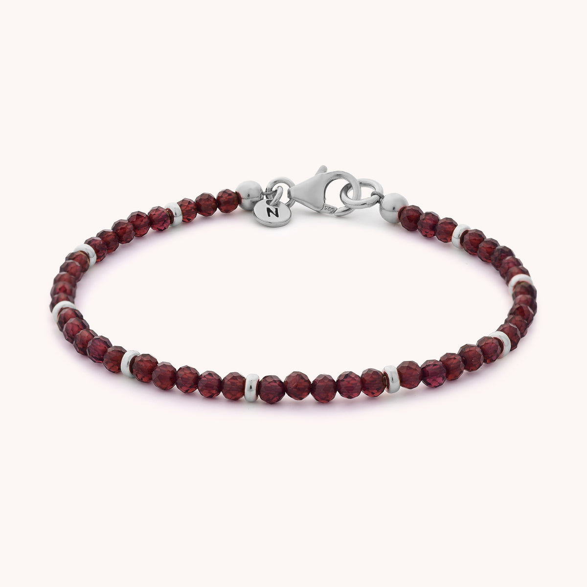 The Garnet Orbit Bracelet - January features delicate round red garnet beads accented with sterling silver spacers, a secure silver lobster clasp, and a small round charm—an elegant accessory that celebrates the January birthstone.