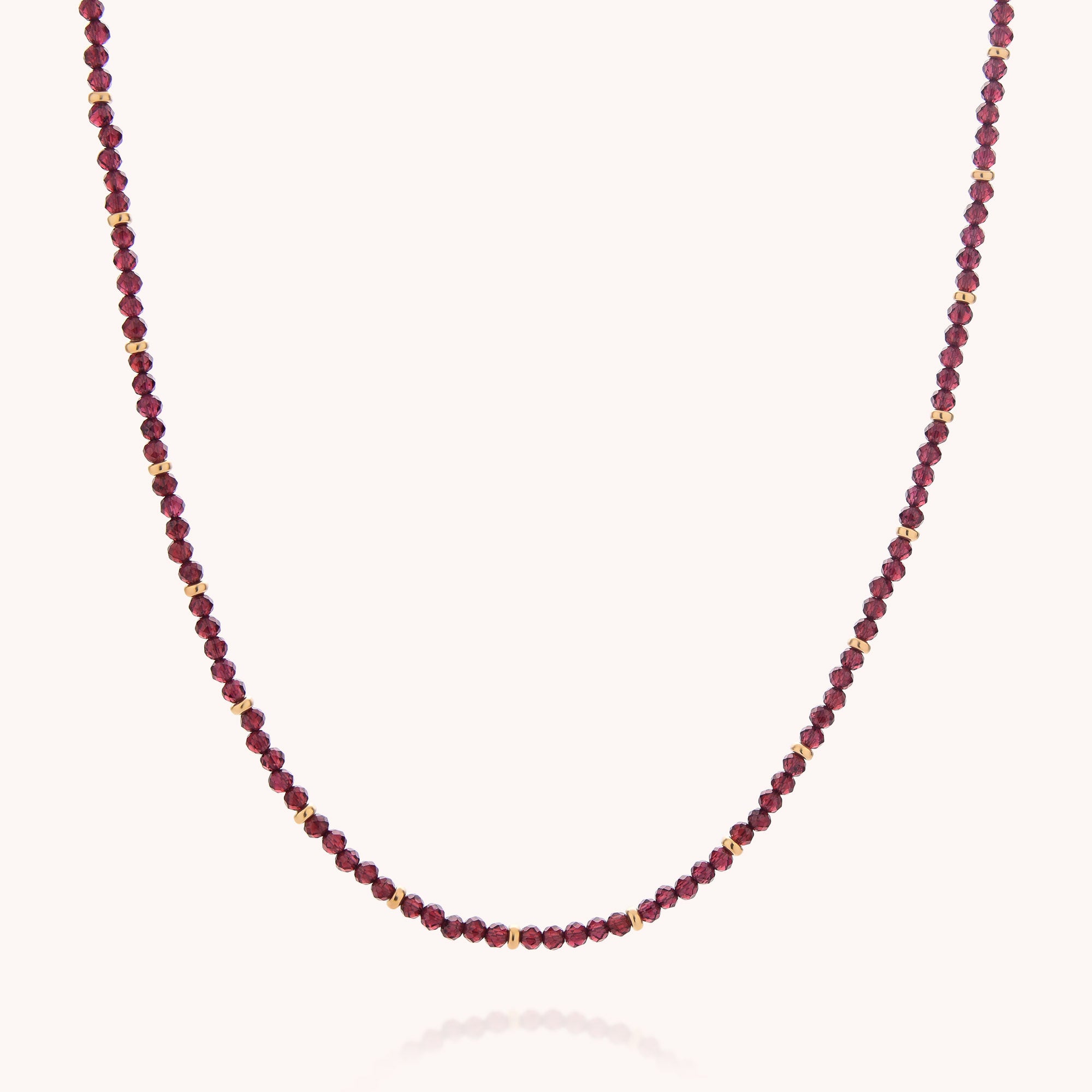 The Garnet Orbit Necklace showcases alternating small red garnet and gold beads, evenly spaced along a delicate chain and presented on a plain white background—ideal for anyone who loves handcrafted jewelry.