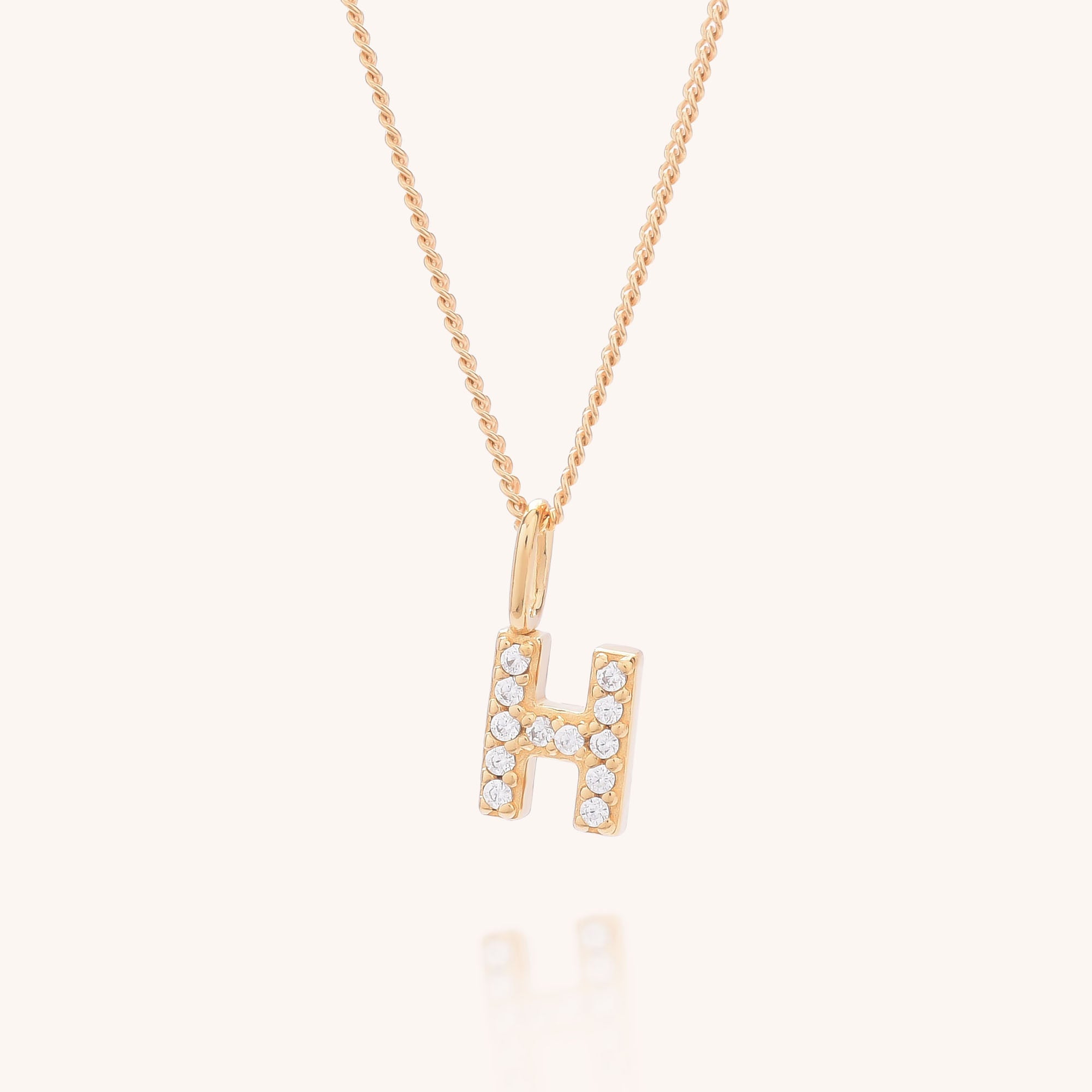The Initial Sparkle Necklace showcases a letter H pendant adorned with sparkling cubic zirconia stones, set against a light, neutral background.