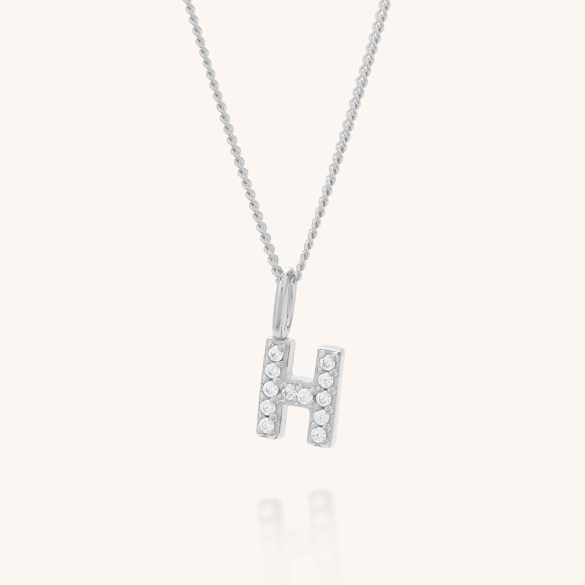 The Initial Sparkle Necklace showcases a silver H-shaped pendant adorned with sparkling cubic zirconia, elegantly displayed against a plain light background.