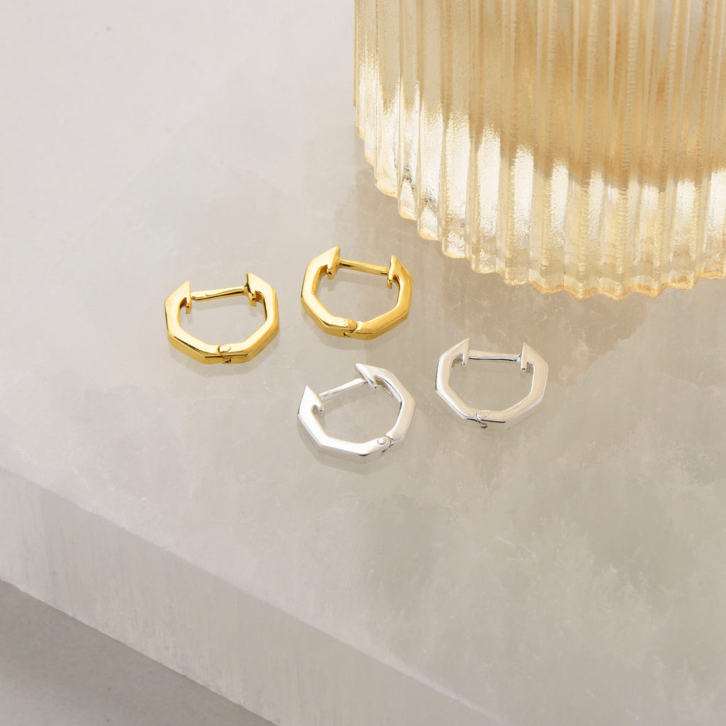hexagon shaped ear hoops in silver and gold next to a vase