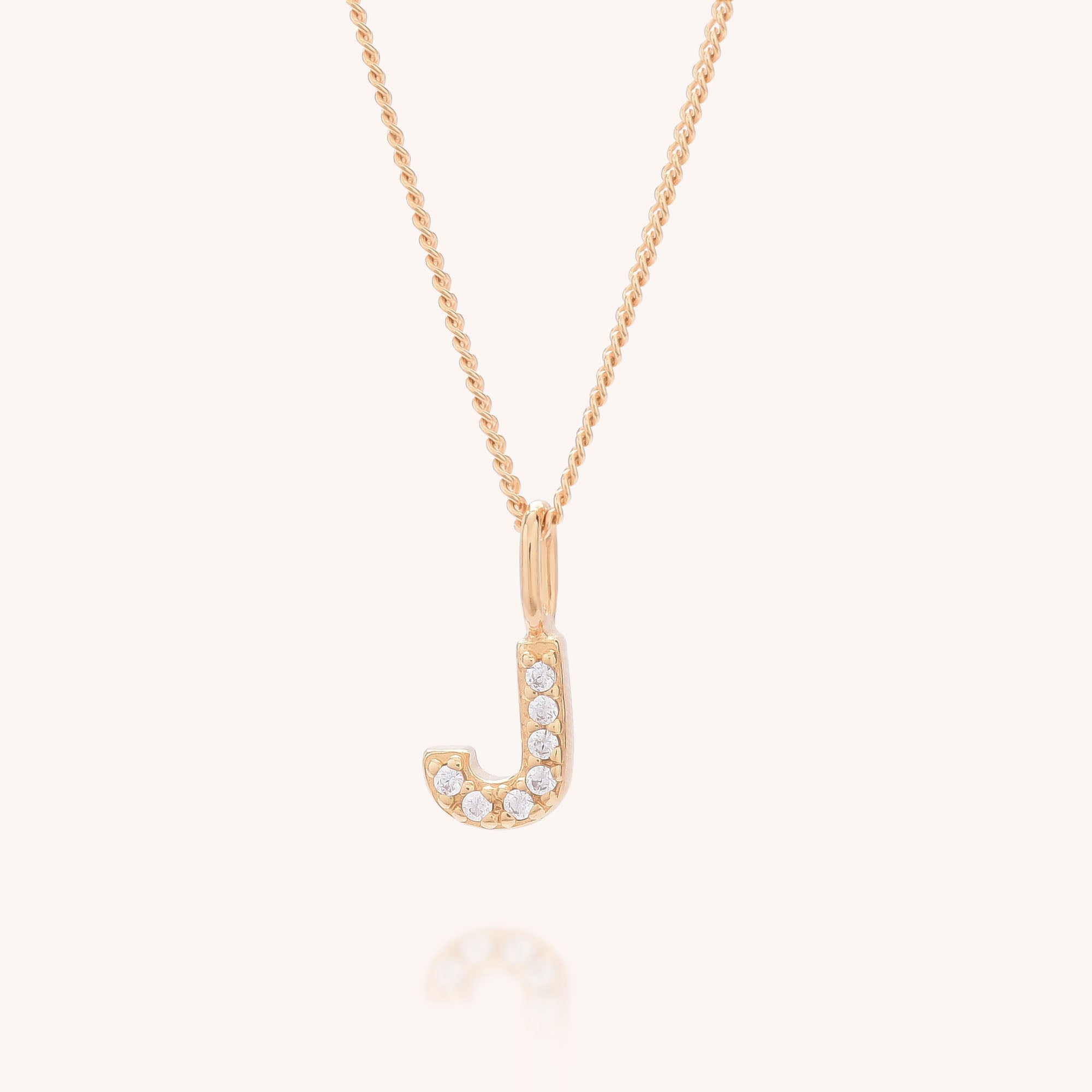 Initial Sparkle Necklace: Elegant gold necklace featuring a J-shaped pendant with shimmering cubic zirconia accents, displayed on a light background.