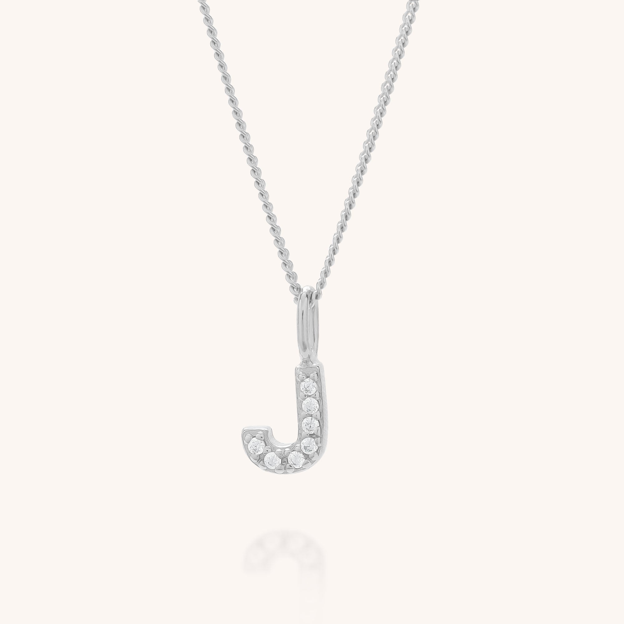The Initial Sparkle Necklace is a silver necklace with a letter J pendant, embellished with sparkling cubic zirconia stones, displayed on a plain light background.