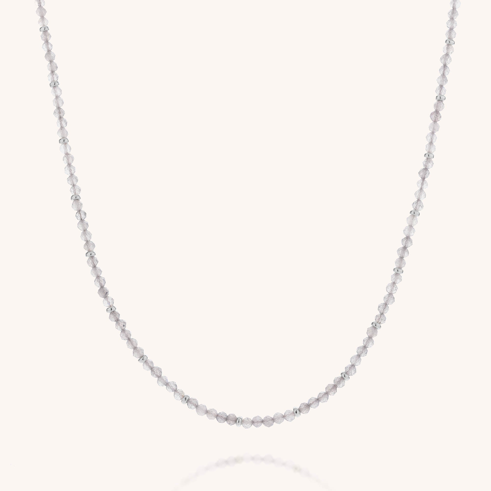 The Labradorite Orbit Necklace is showcased against a plain white background in a graceful curve, featuring faceted labradorite beads delicately spaced along the sterling silver design to create a touch of subtle iridescence.