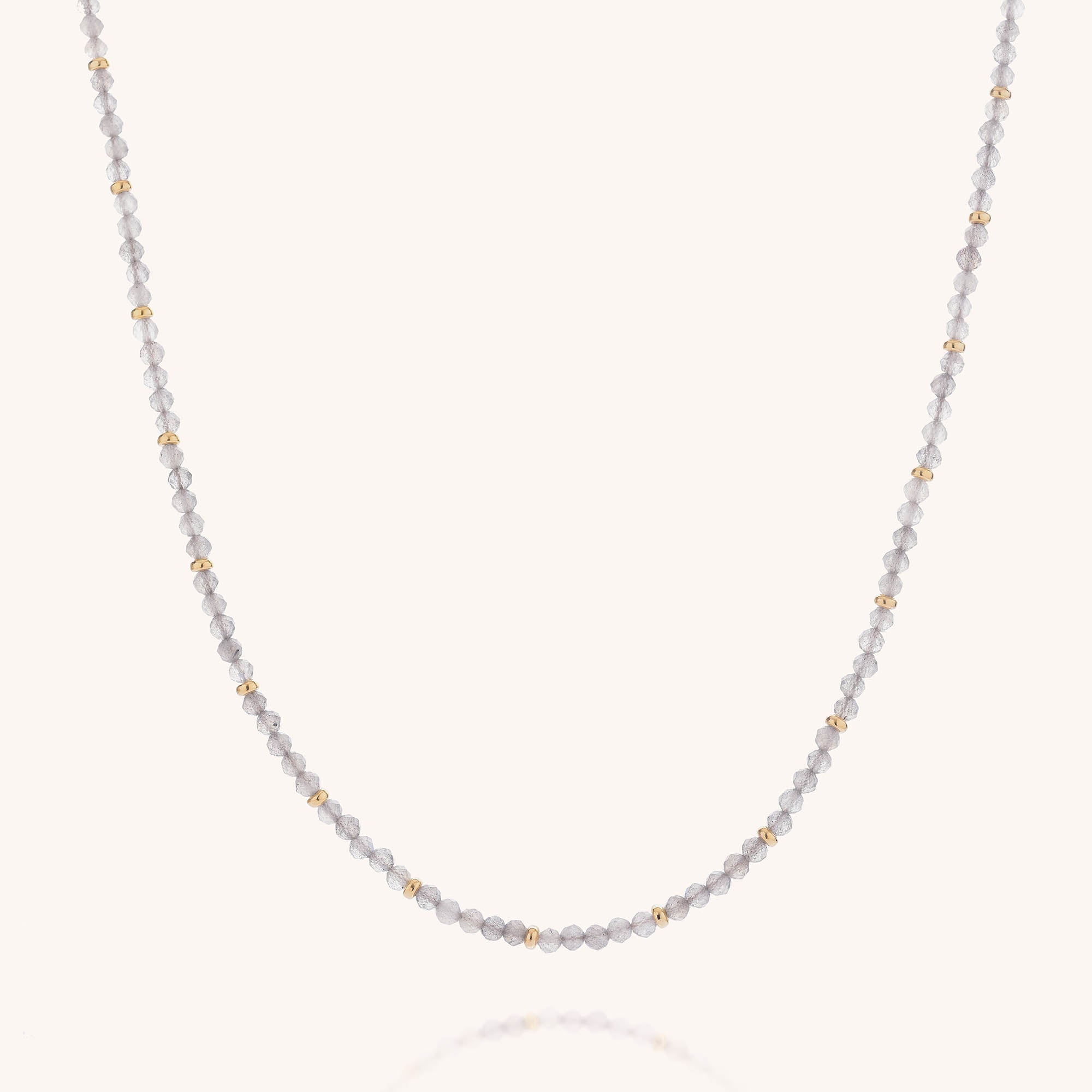 Introducing the Labradorite Orbit Necklace: a delicate accessory featuring small, round, light gray faceted labradorite beads accented with evenly spaced gold beads, beautifully displayed on a simple, light background.