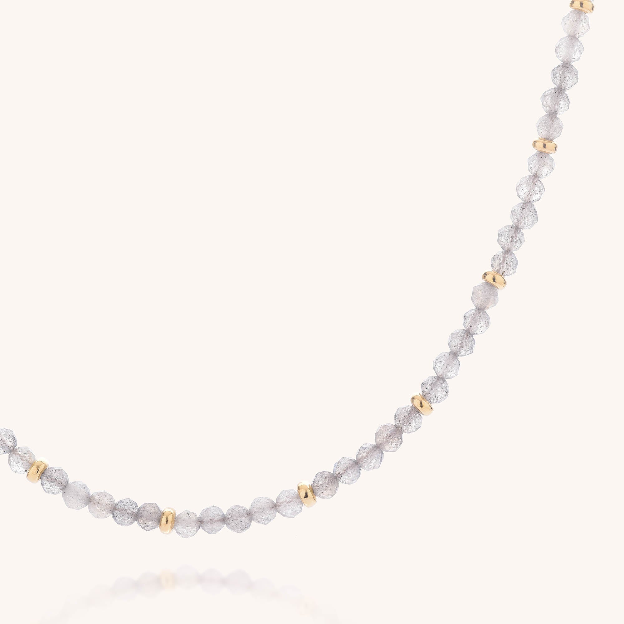 Close-up of the Labradorite Orbit Necklace, showcasing small, round faceted labradorite beads accented with spaced gold details on a plain, light background.