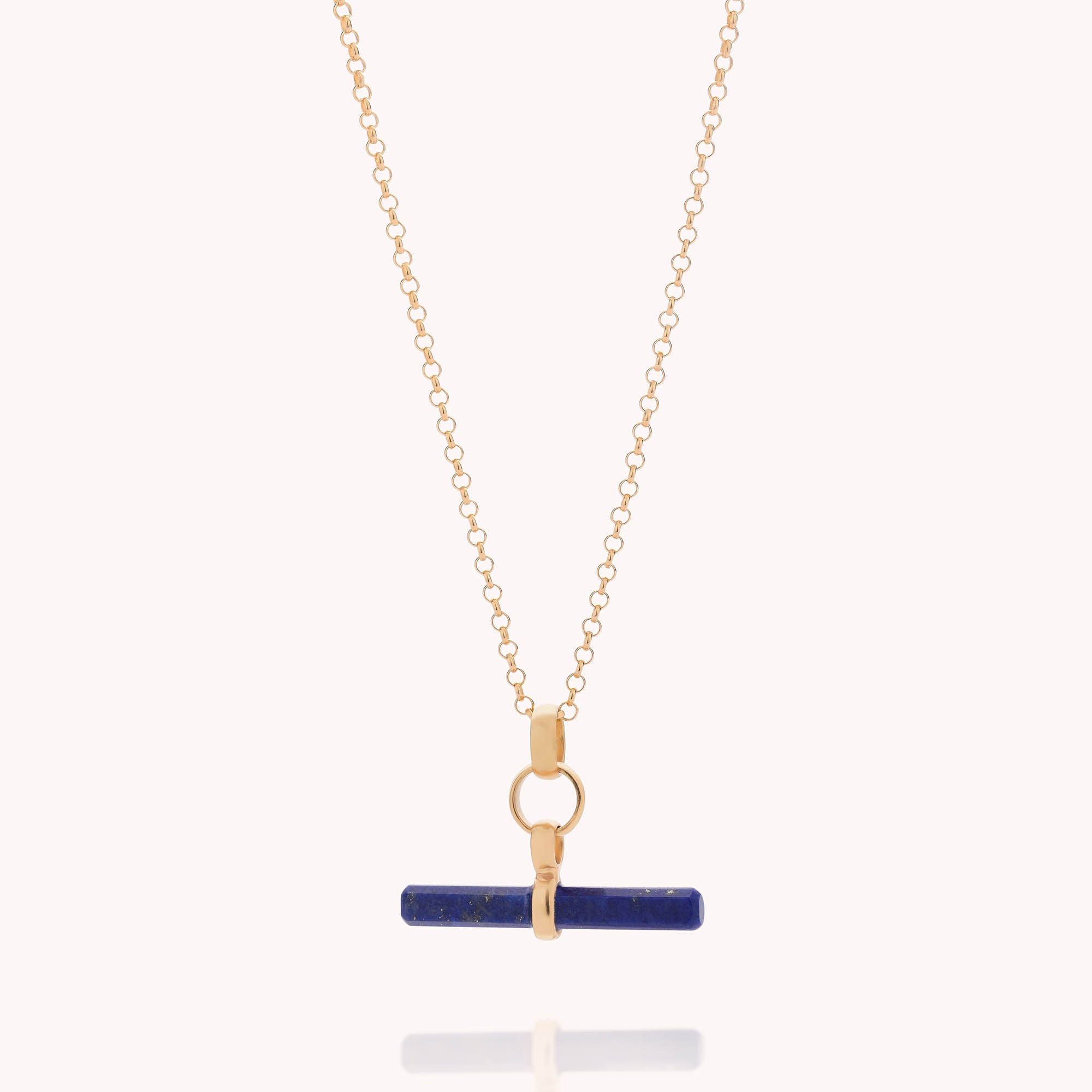 The Gemstone T Bar Necklace features a gold chain with a horizontal blue bar pendant and a circular gold clasp, showcased against a light background.