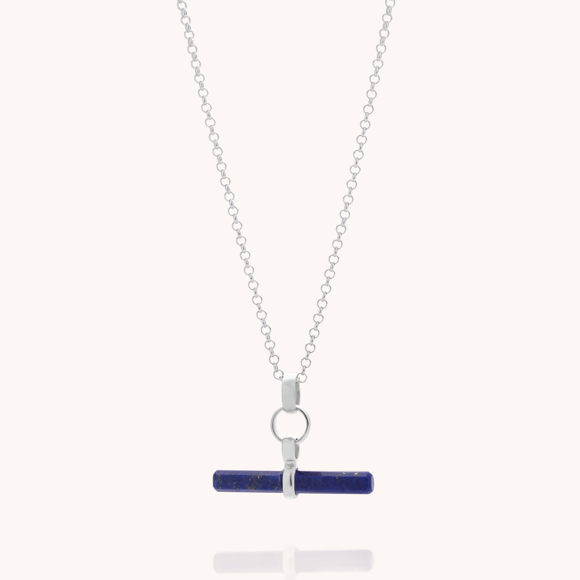 Introducing the Lapis T-Bar Necklace: a sterling silver chain necklace featuring a horizontal, cylindrical lapis lazuli gemstone pendant in a sleek T-bar design, elegantly attached by silver loops and showcased against a light background.