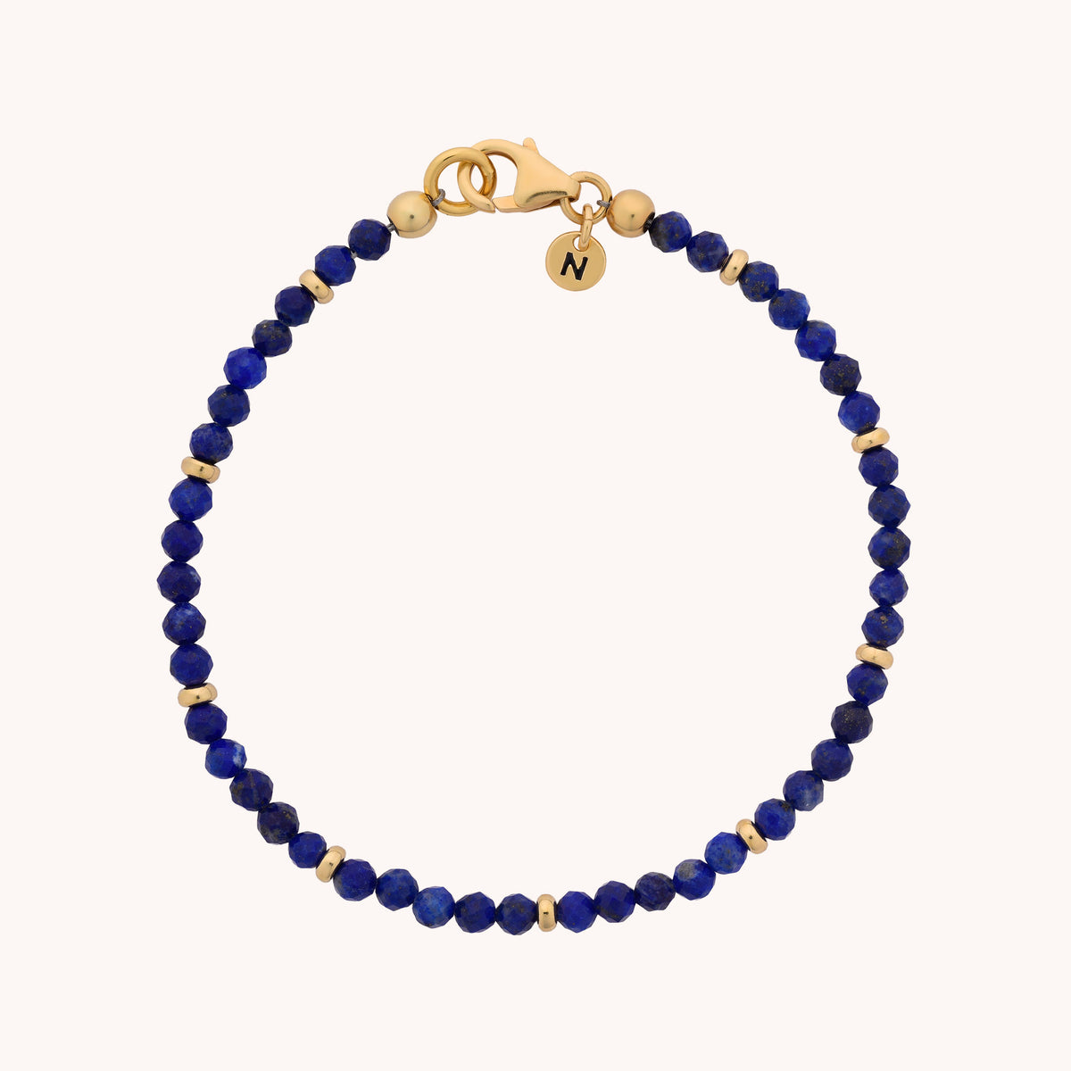 The Lapis Orbit Bracelet - September showcases round blue lapis lazuli beads accented with small gold spacers, finished with a gold lobster clasp and a petite round charm engraved with the letter N.