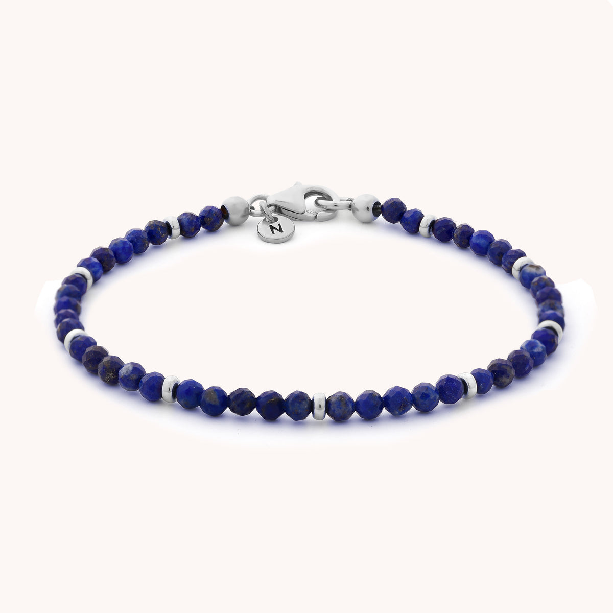 Introducing the Lapis Orbit Bracelet - September: a delicate bracelet featuring small, faceted lapis lazuli beads and silver spacers, finished with a silver clasp and a round charm engraved with the letter N. This stunning gemstone bracelet makes a thoughtful gift, especially for anyone celebrating a September birthday.