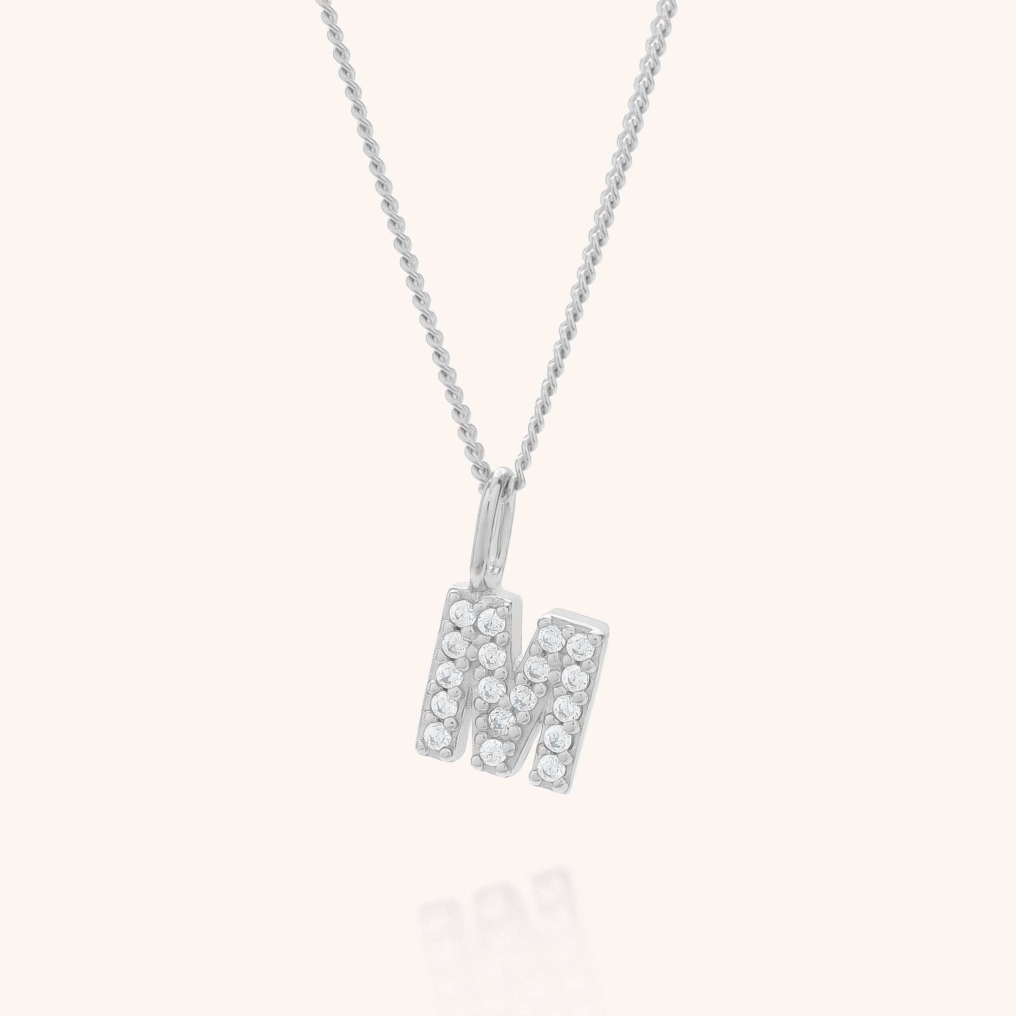The Initial Sparkle Necklace showcases a silver pendant shaped like the letter M, encrusted with sparkling cubic zirconia stones, and is presented on a simple light background.