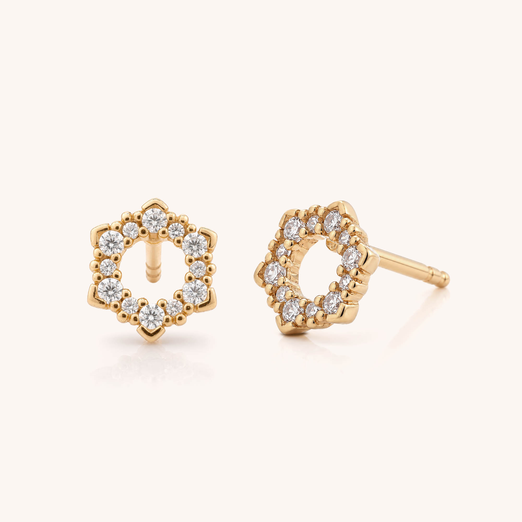 Hexa Stud Earrings feature a floral-inspired hexagonal design, each stud adorned with small round white diamonds encircling the center for an elegant touch. These geometric gold earrings are showcased on a neutral background.