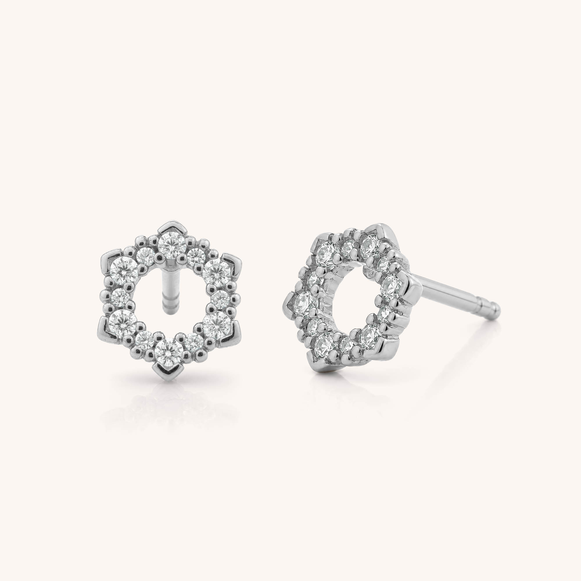Two Hexa Stud Earrings in silver, each featuring a delicate open circle design with intricate, flower-inspired patterns and adorned with sparkling clear cubic zirconia stones, displayed against a plain light background.